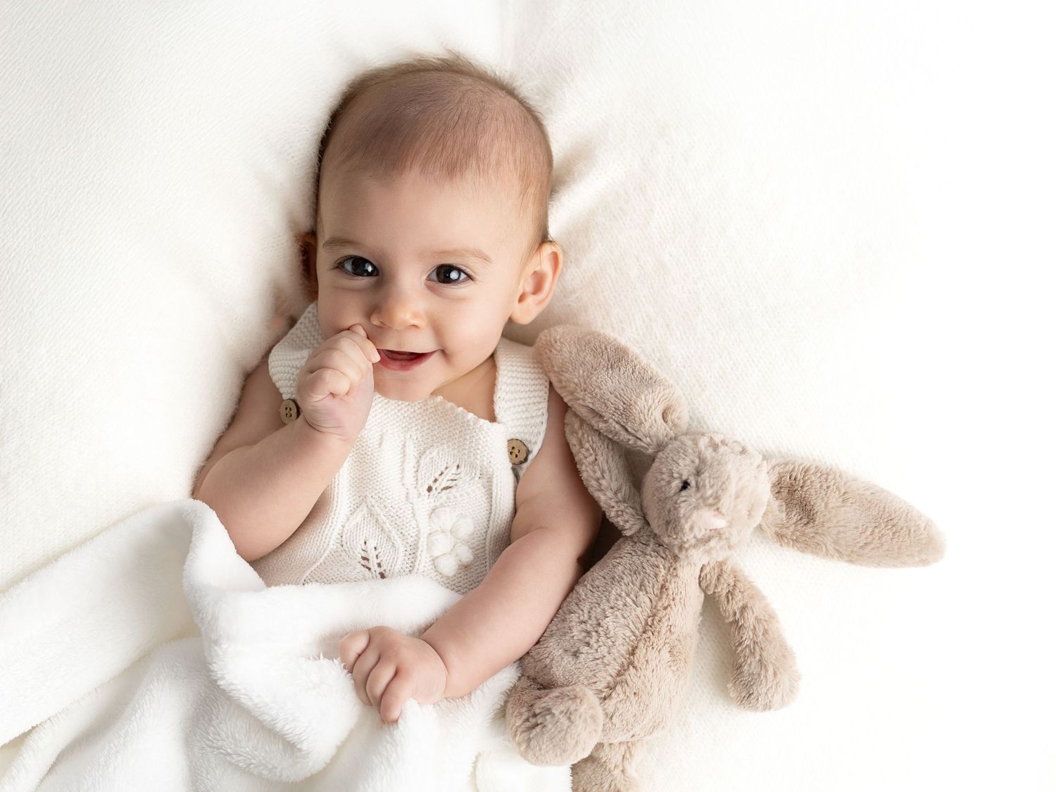 Happy baby playing with plush toy on white background.