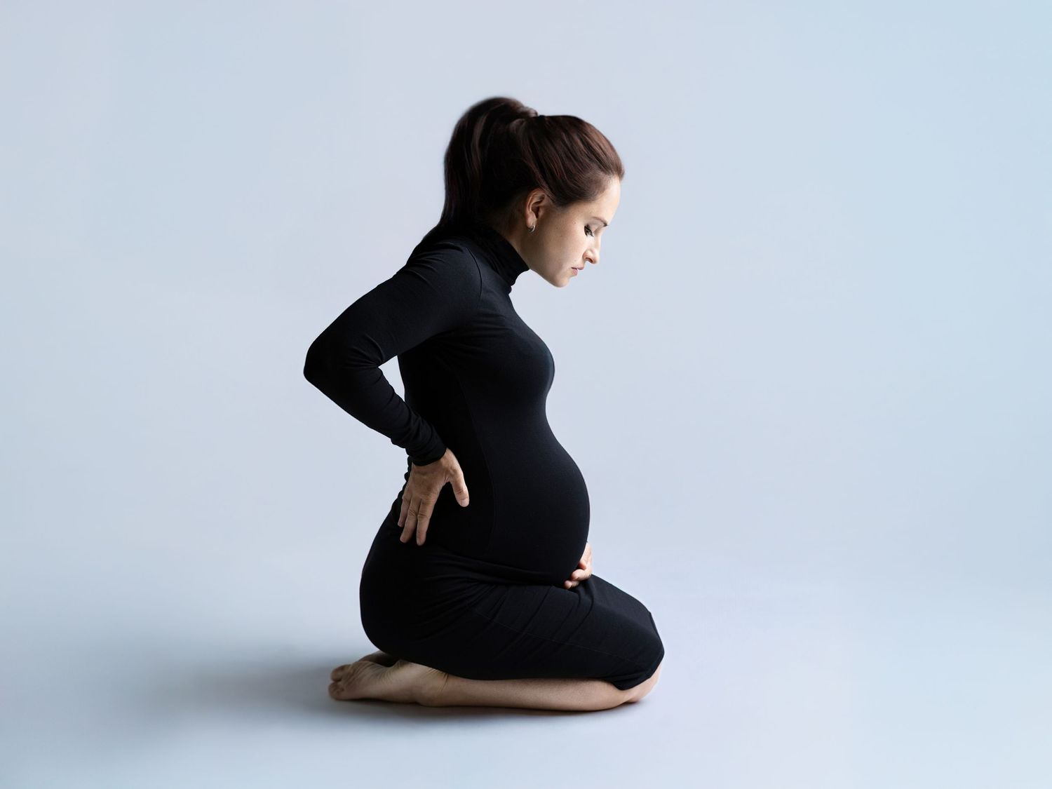 Silhouette of pregnant woman in black dress poses gracefully against light backdrop.