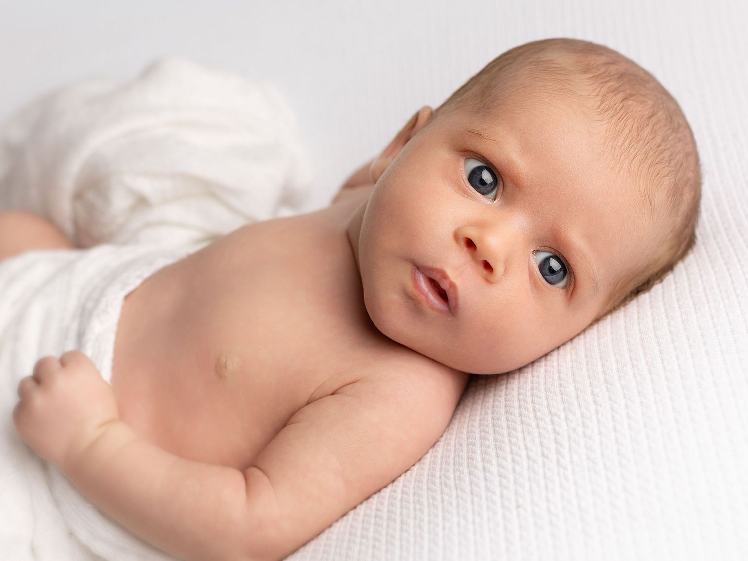Series of artistic close-up portraits of a baby lying on textured white fabric.