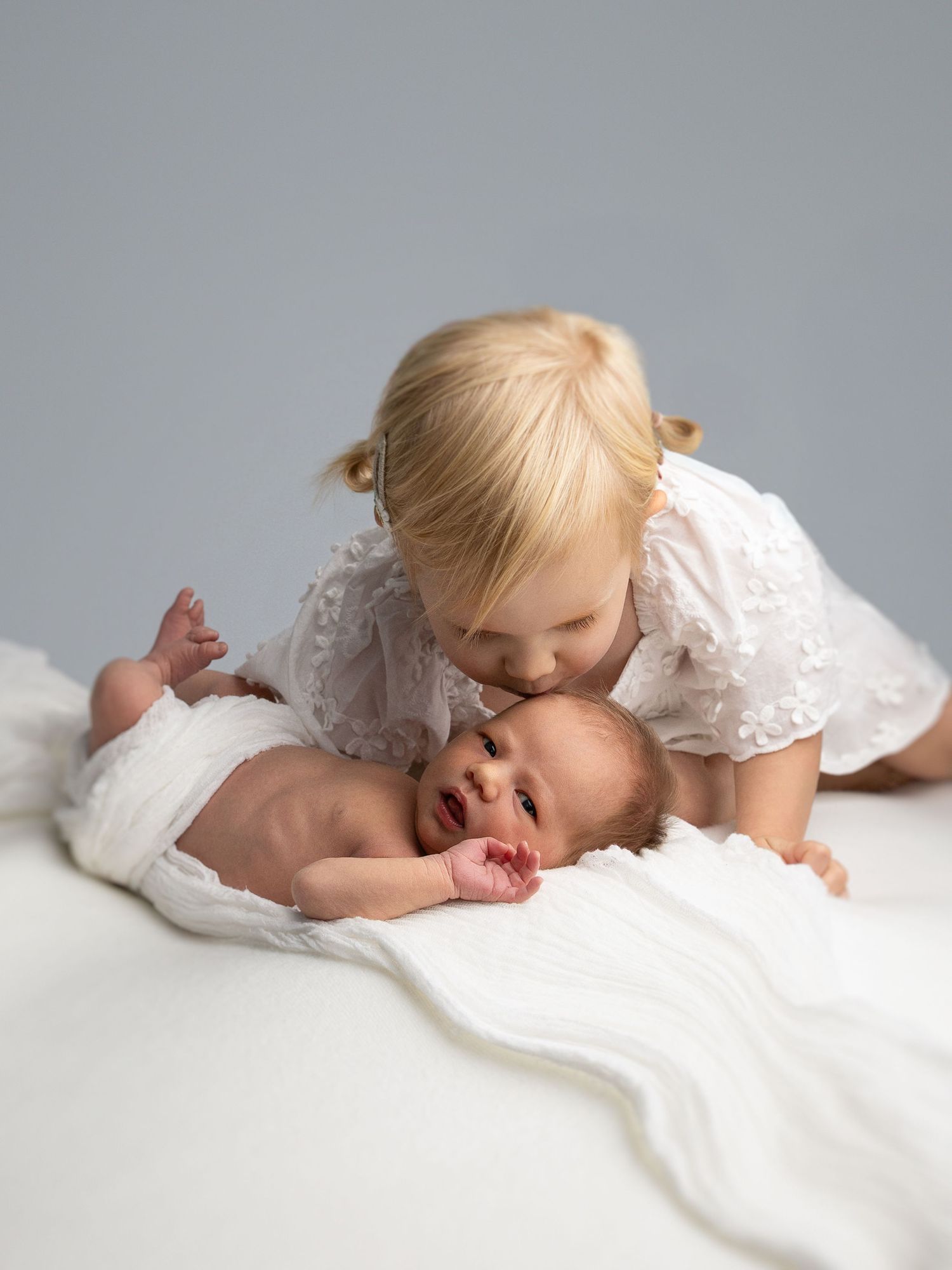 Child in white lace dress resting on soft white surface.