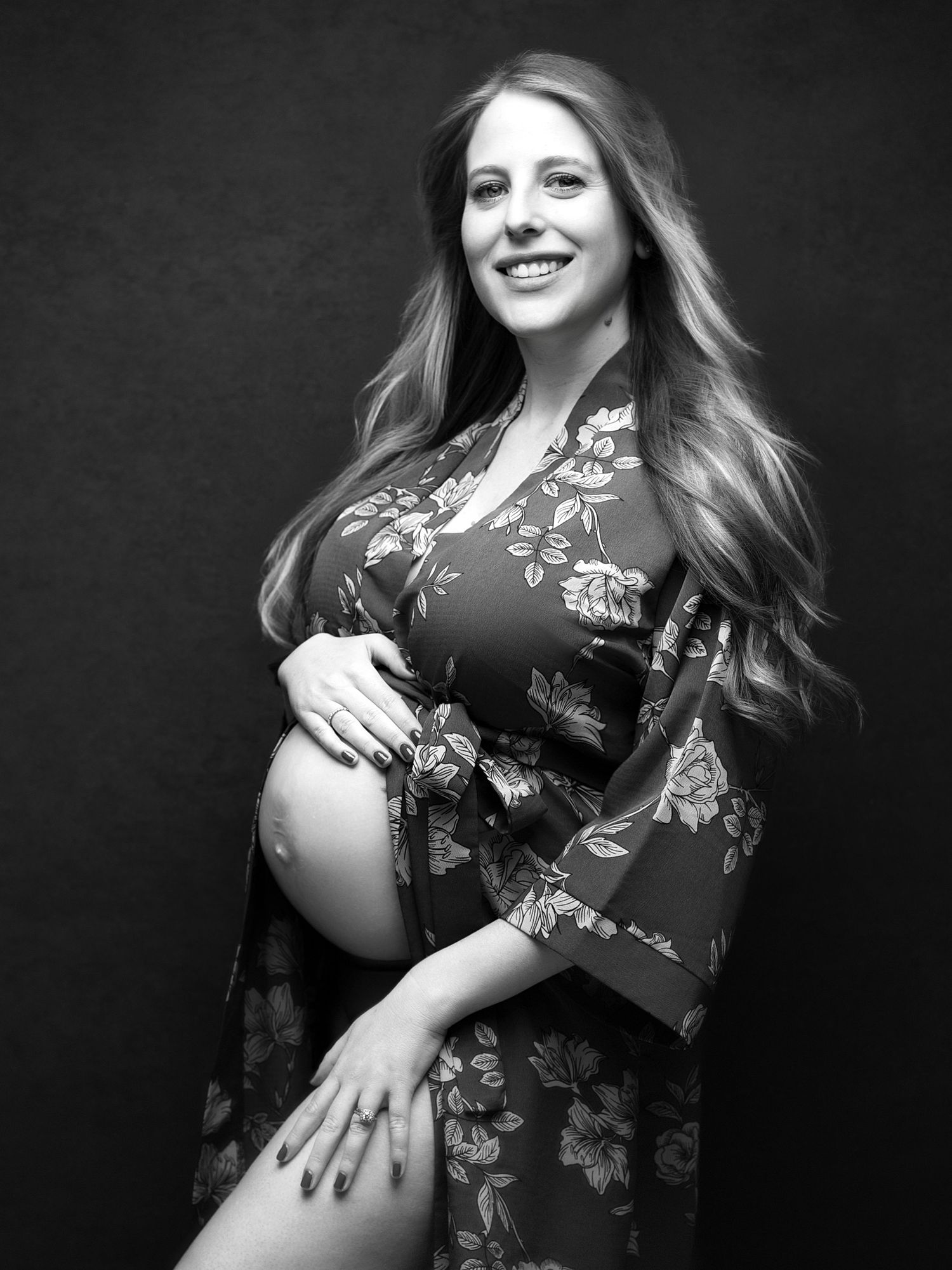 Black and white maternity portrait in floral dress showing pregnant belly.