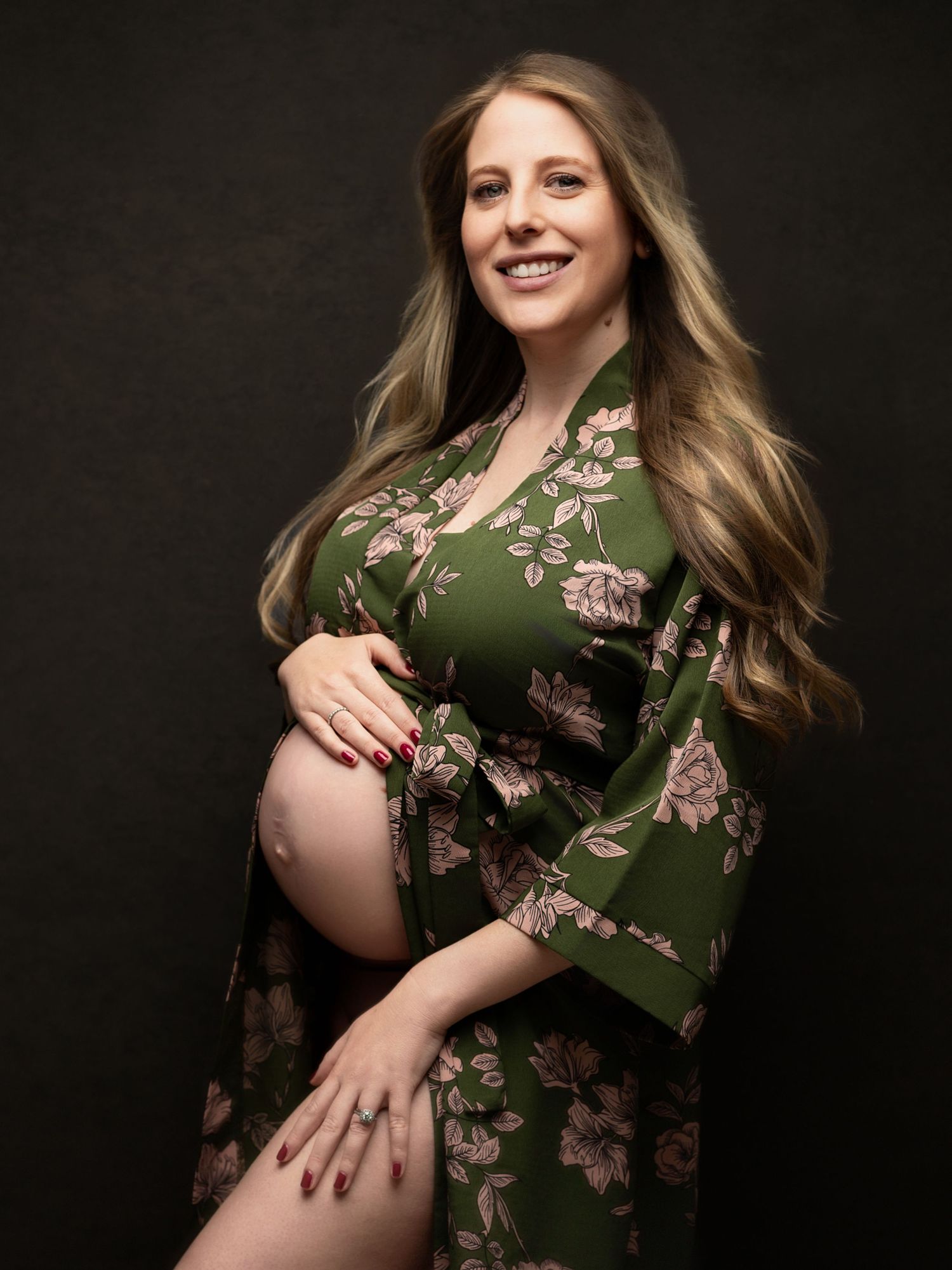 Maternity photoshoot featuring green floral dress against dark background.