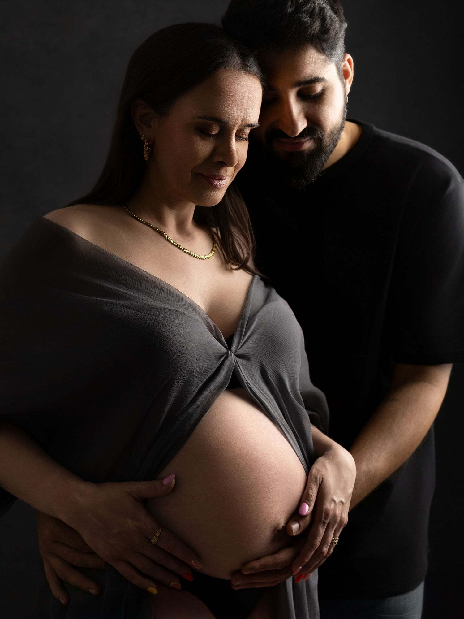 Dramatic maternity photos showing couple embracing in dark setting.
