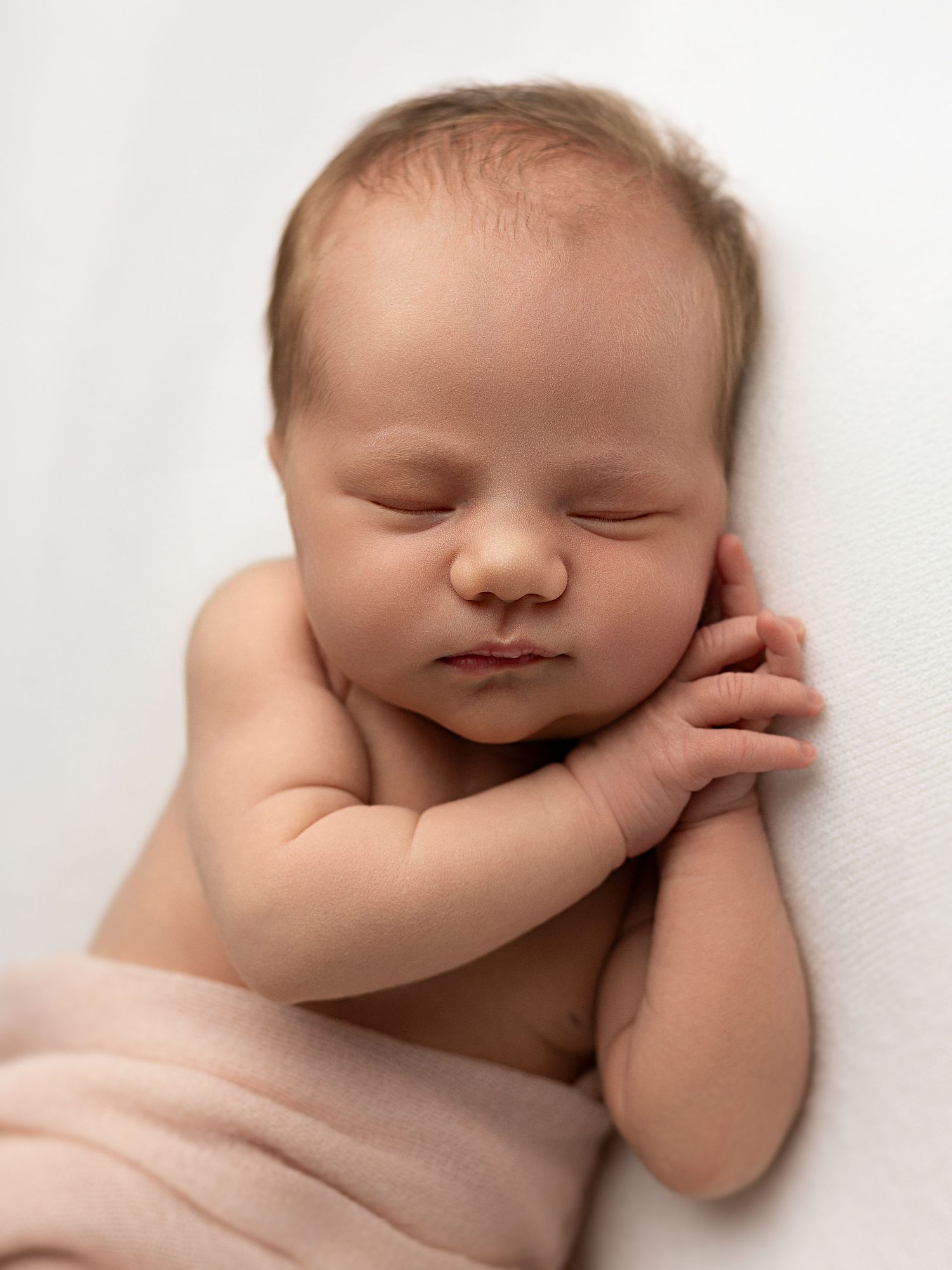 Peaceful sleeping newborn baby in soft white blanket against neutral background.