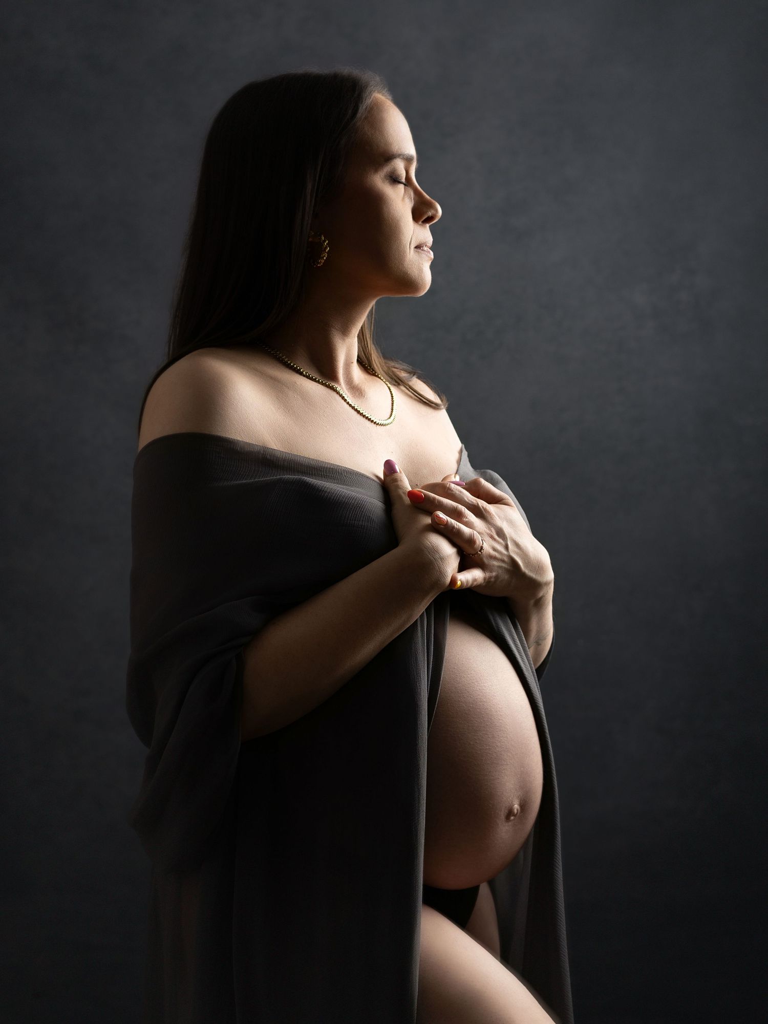 Side view maternity silhouette with dramatic lighting and dark fabric draping.