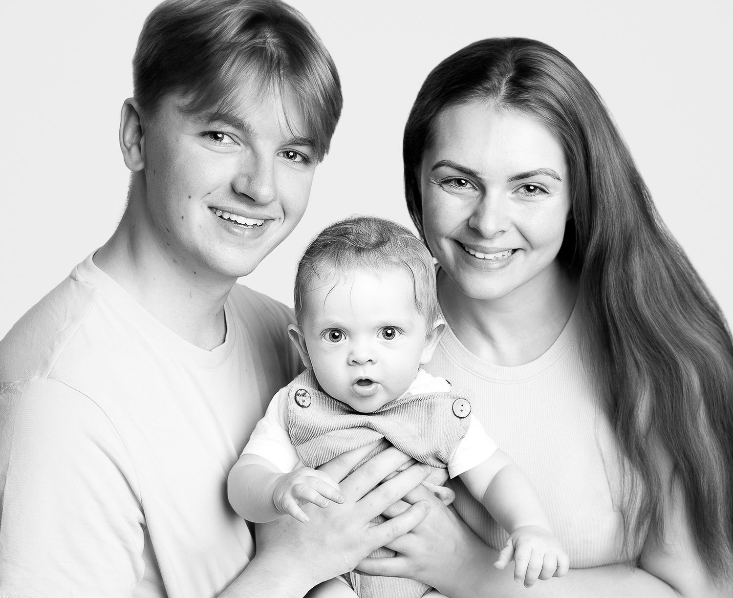 Black and white portrait of smiling young couple holding their newborn baby, family photo studio shot.