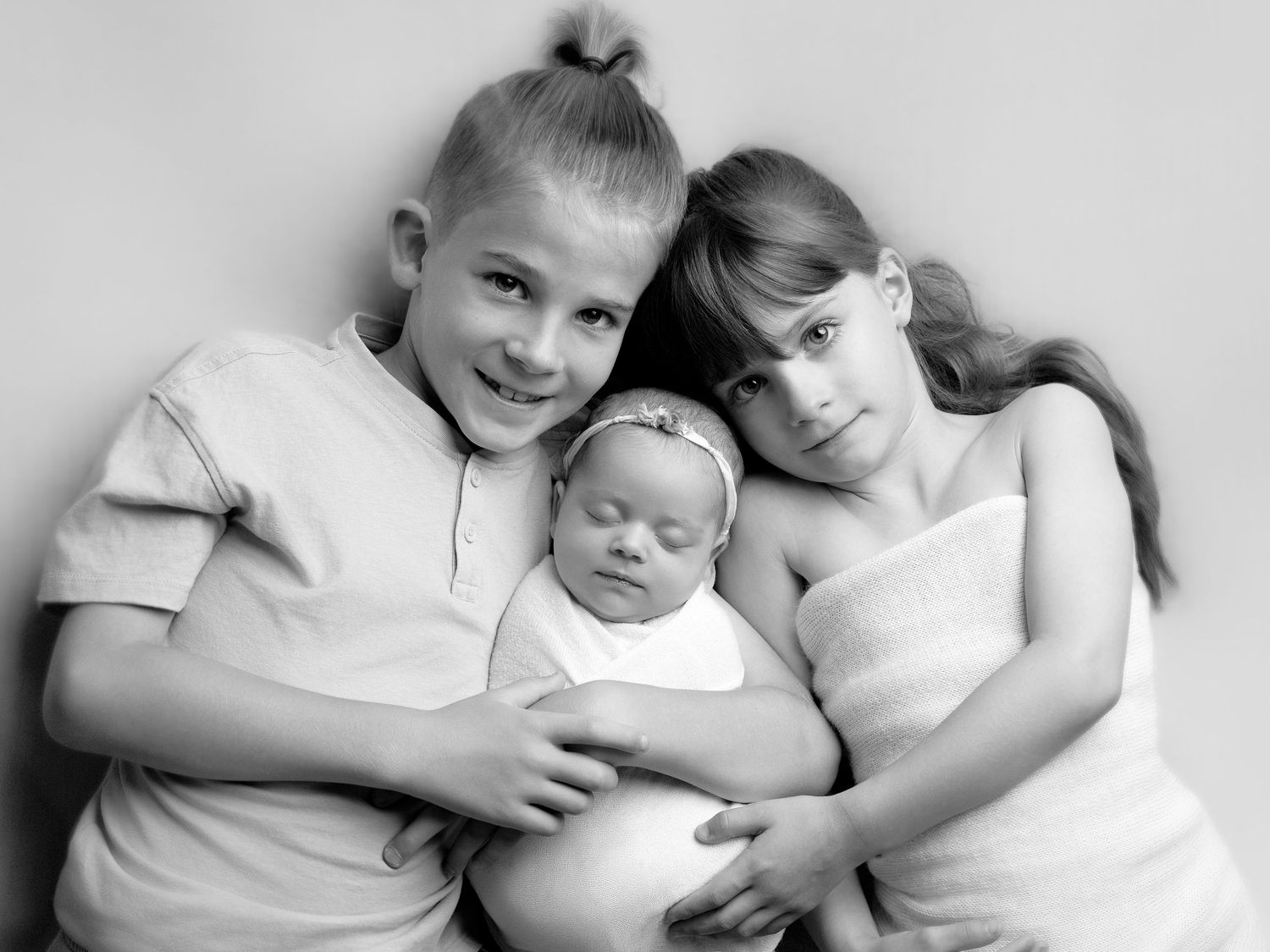 Black and white portrait of two children lovingly holding a sleeping newborn baby sibling.