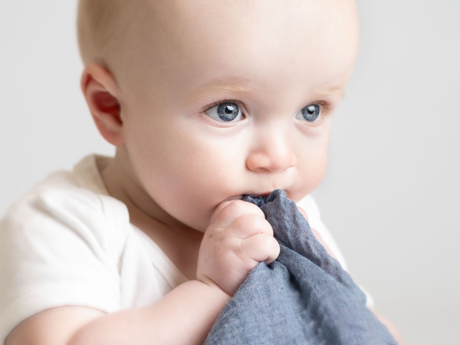 Close up view of baby chewing on gray teething toy while wearing white onesie.