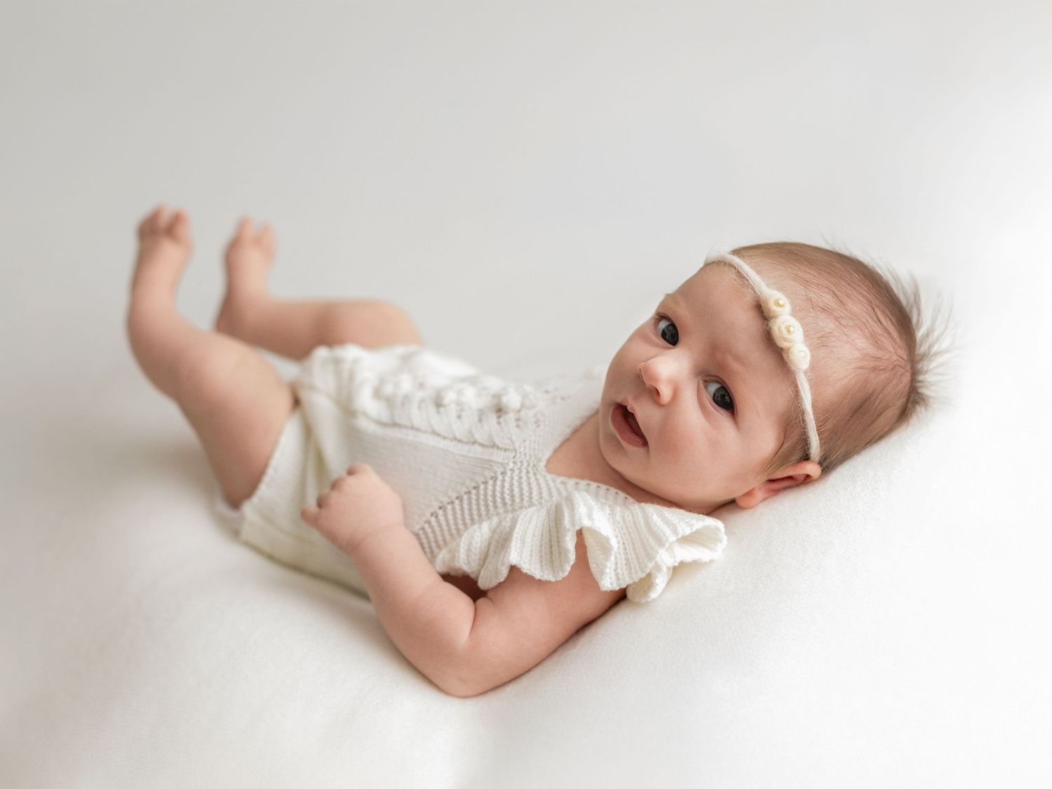 Baby wearing white clothing photographed in various natural poses on light background.