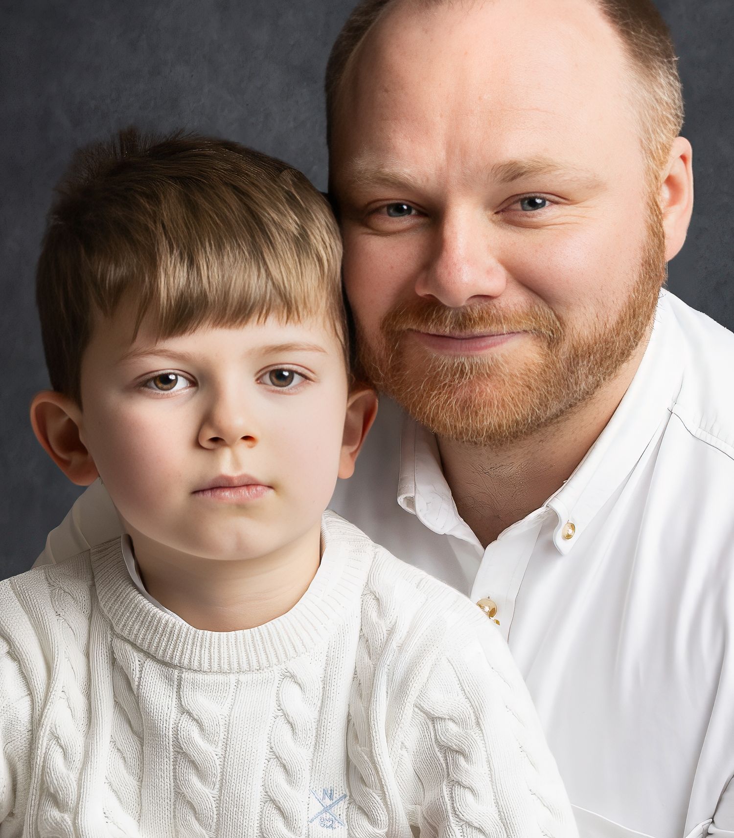 Portrait of a man with a red beard and young boy in matching white cable-knit sweaters posing together.