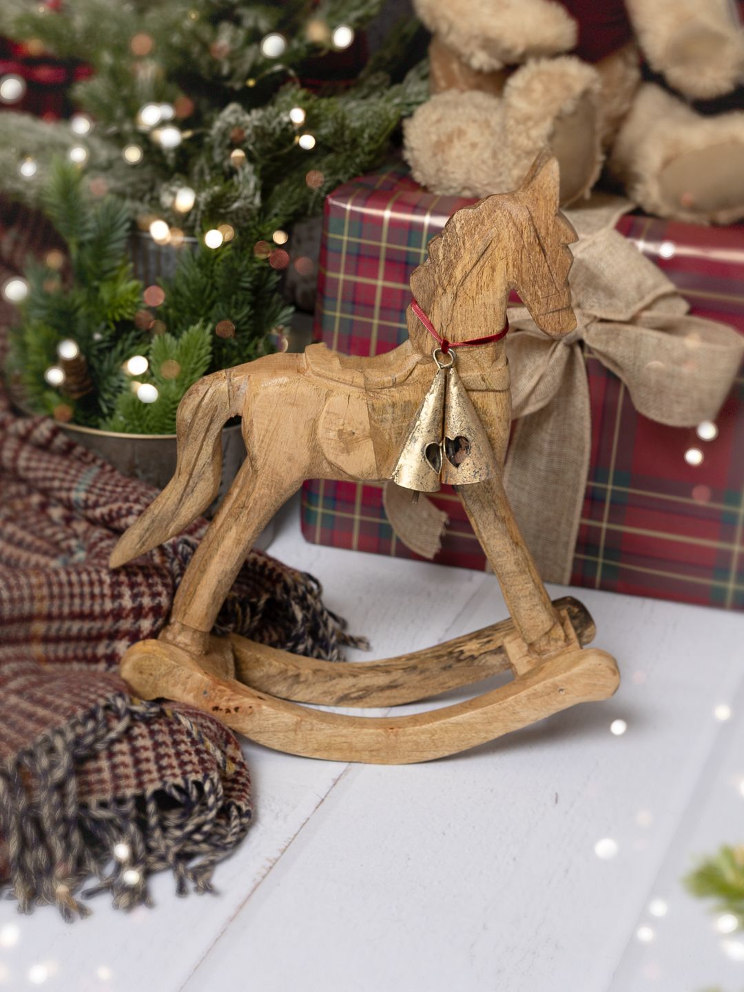 Vintage wooden rocking horse toy with gold bell and bow, displayed in a festive Christmas setting with gifts and greenery.