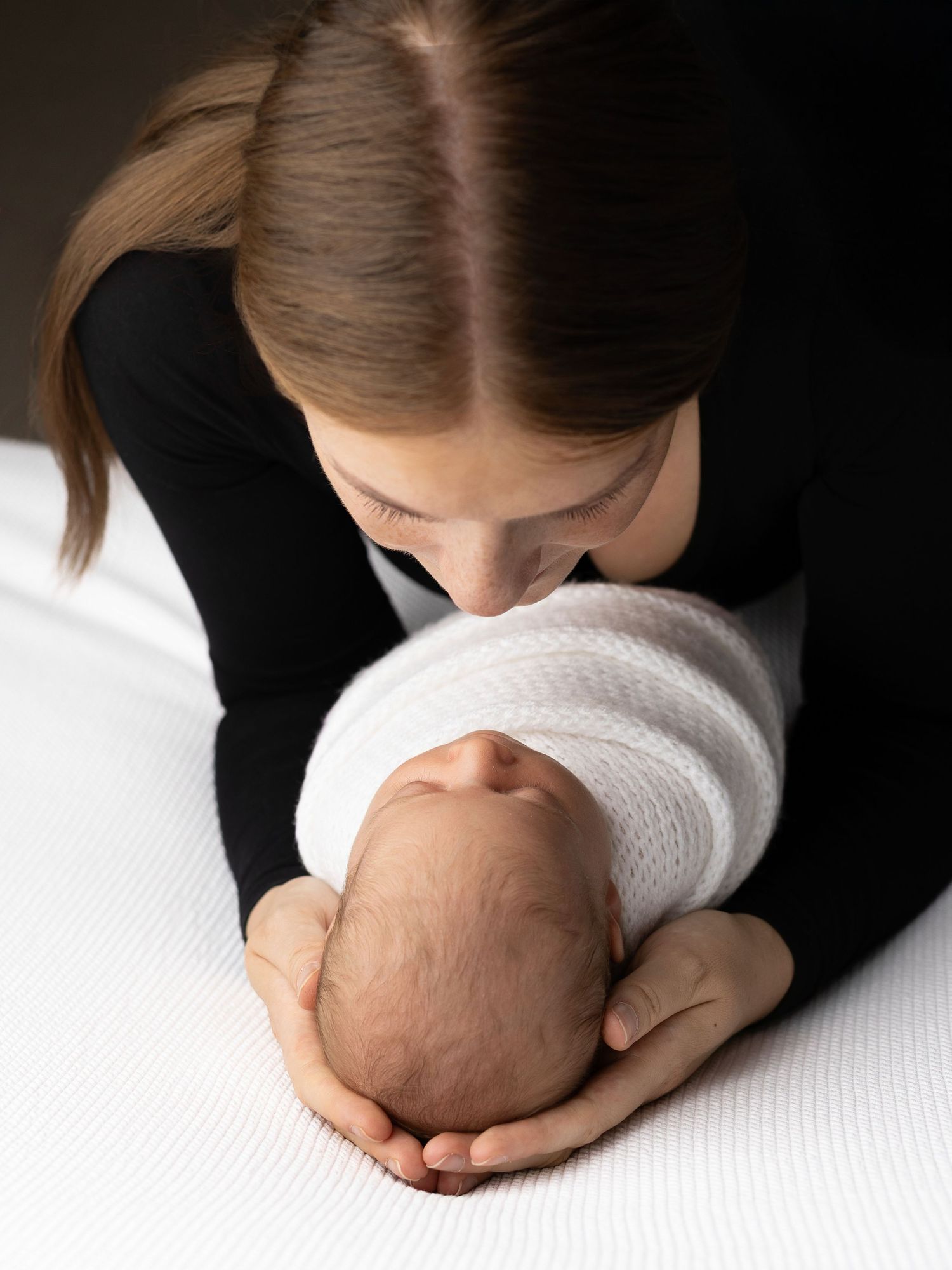 Intimate color portrait of parent cradling newborn wrapped in white fabric.