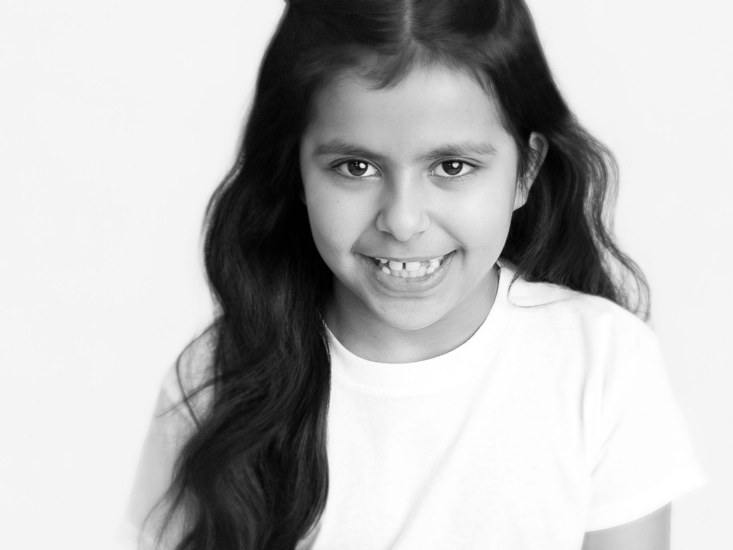 Black and white portrait of a smiling young girl with long dark hair wearing a white t-shirt.