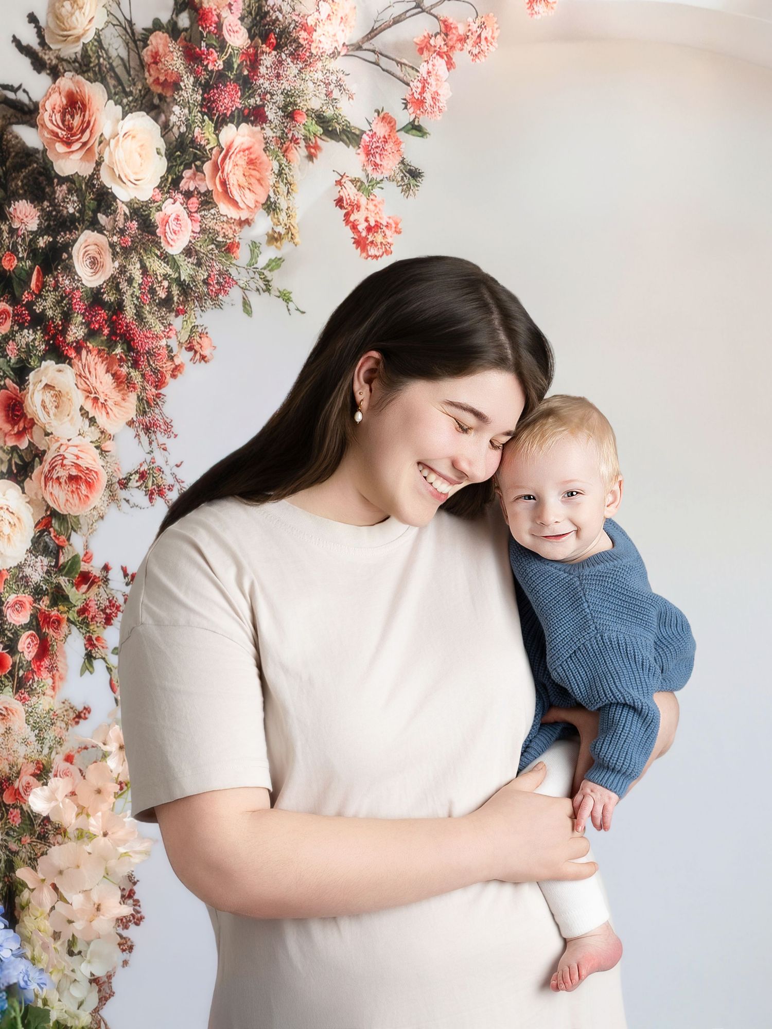 A tender moment captured in a floral studio setting with pink and peach roses creating a romantic backdrop.