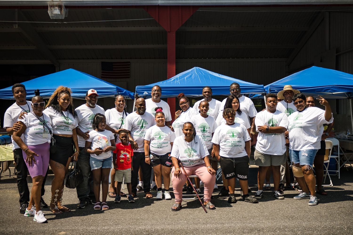 A large group of people in matching family reunion t-shirts pose together under blue tents.