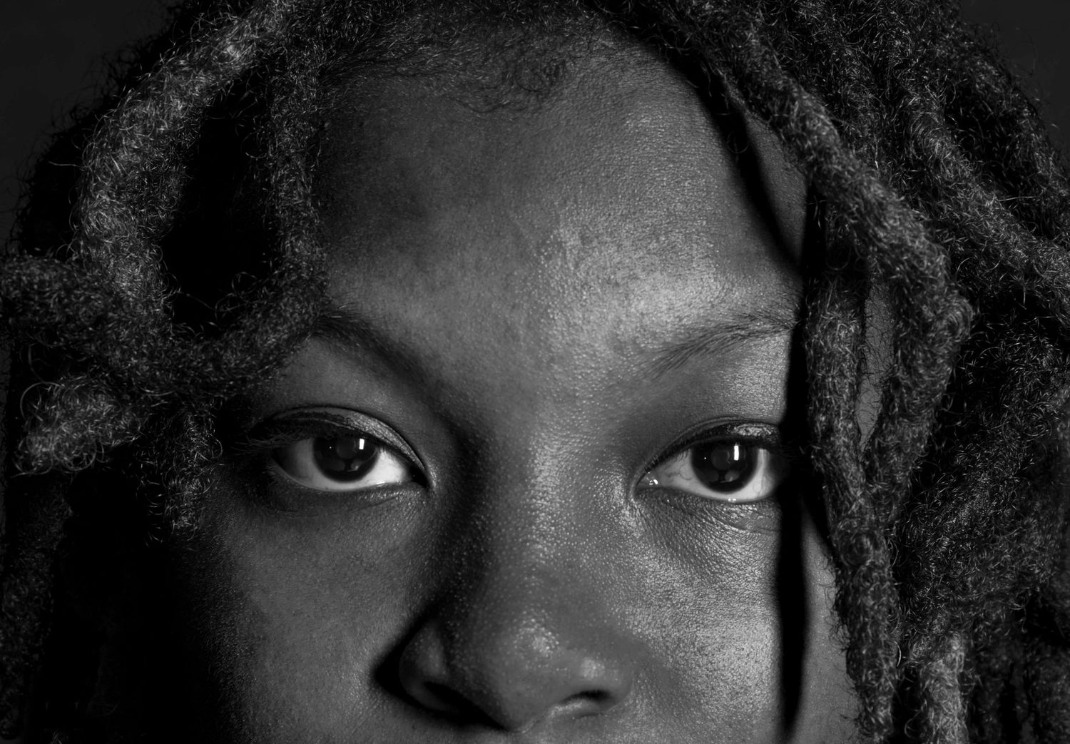 Close-up black and white portrait of Black person with locs showing intense expressive eyes.