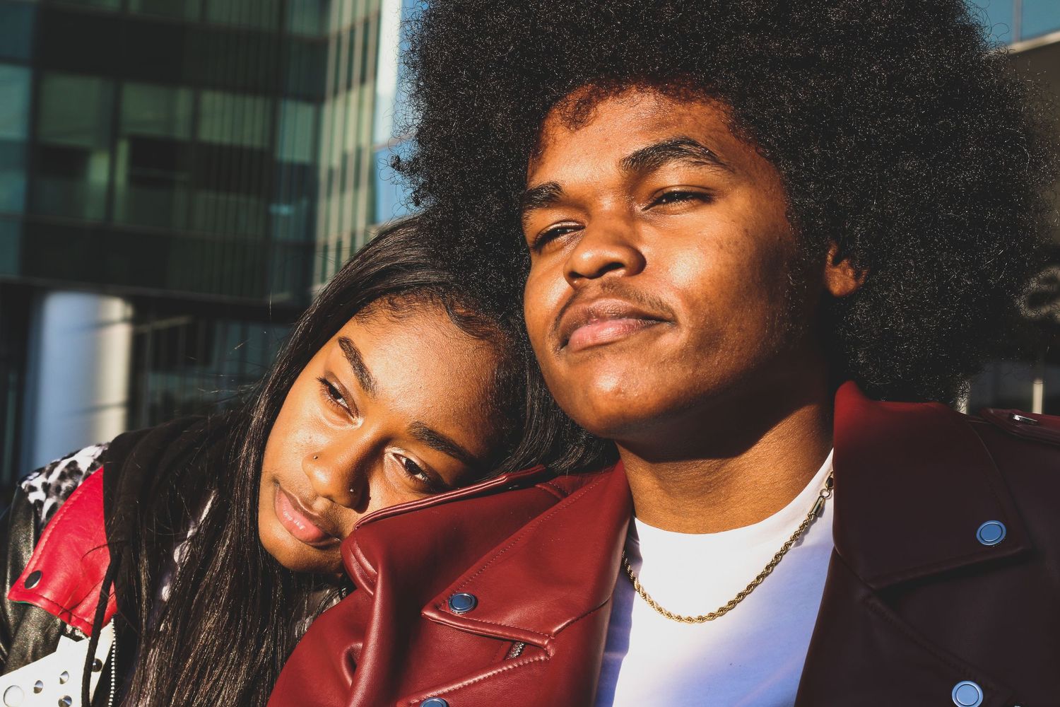 Close-up portrait of a young Black couple in red leather jackets outdoors.