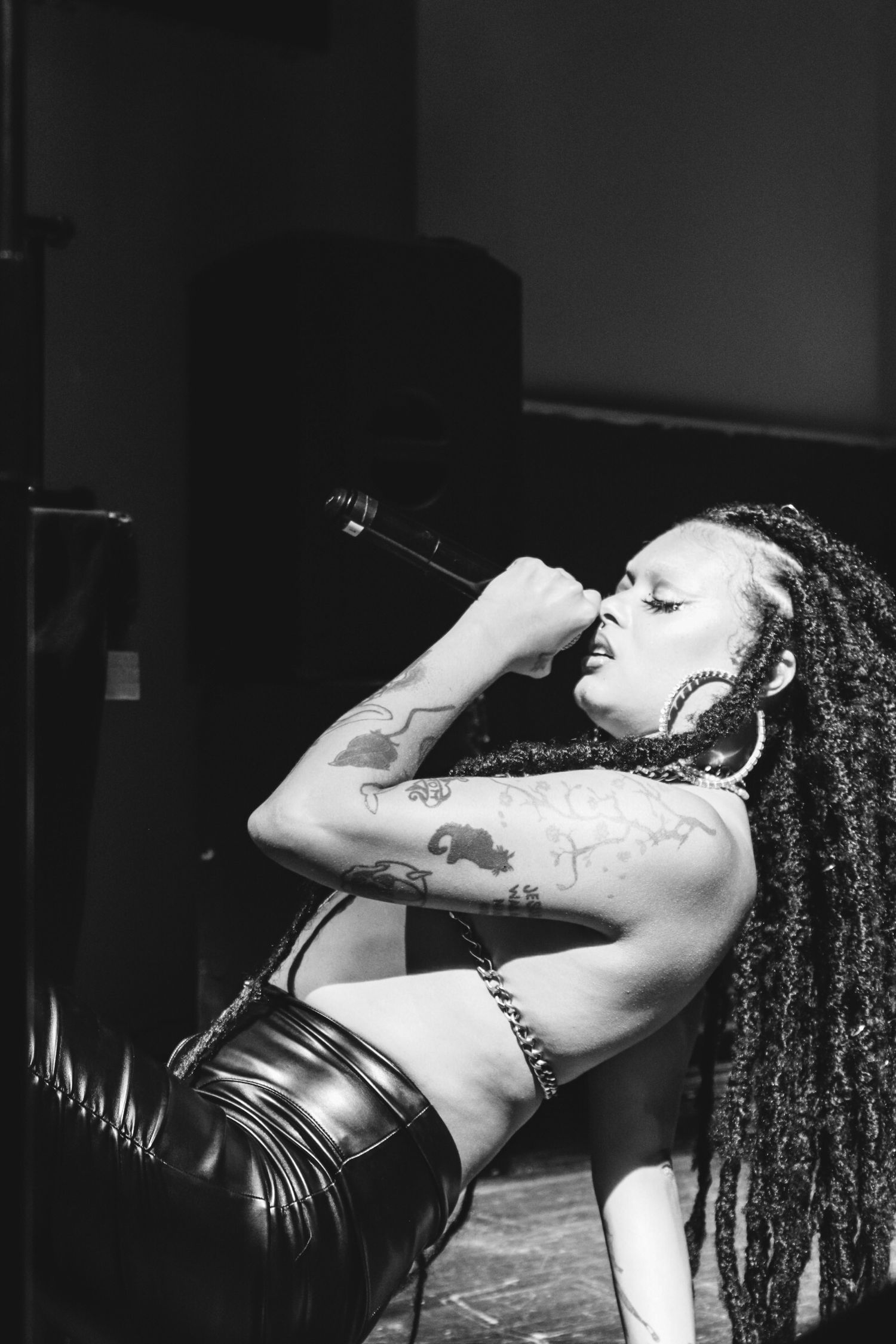 Black and white photo of tattooed performer singing into microphone on stage.