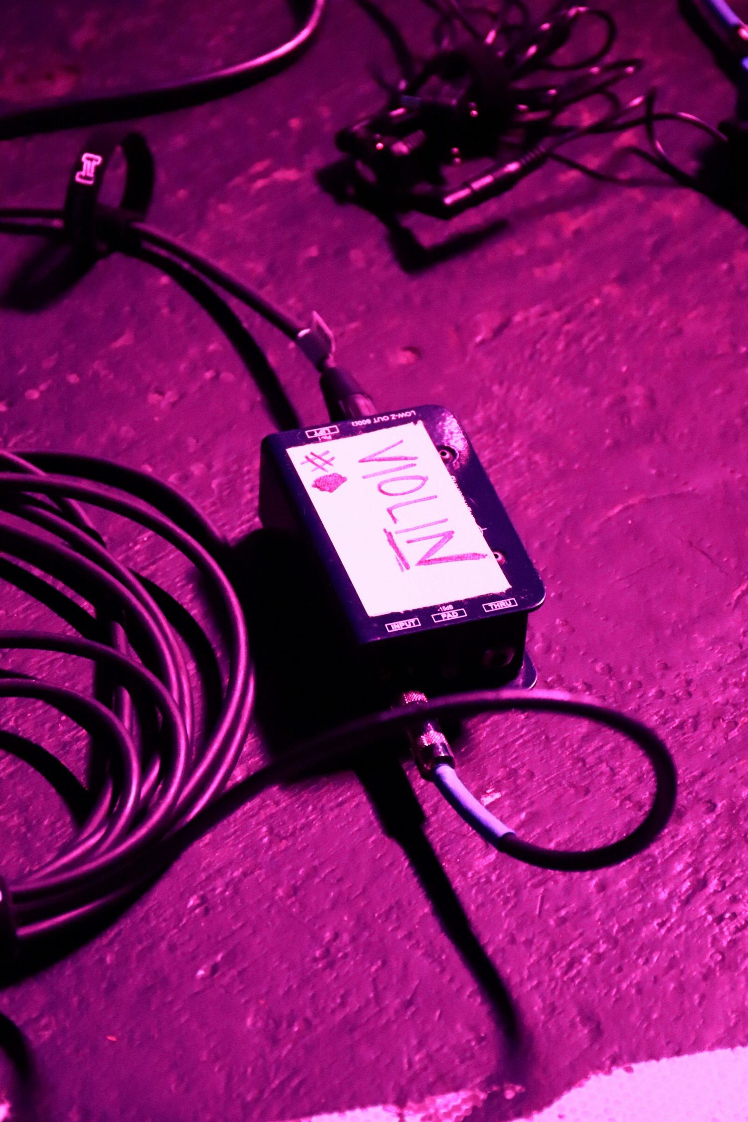 Audio equipment labeled VIOLIN with cables on purple-lit stage floor.