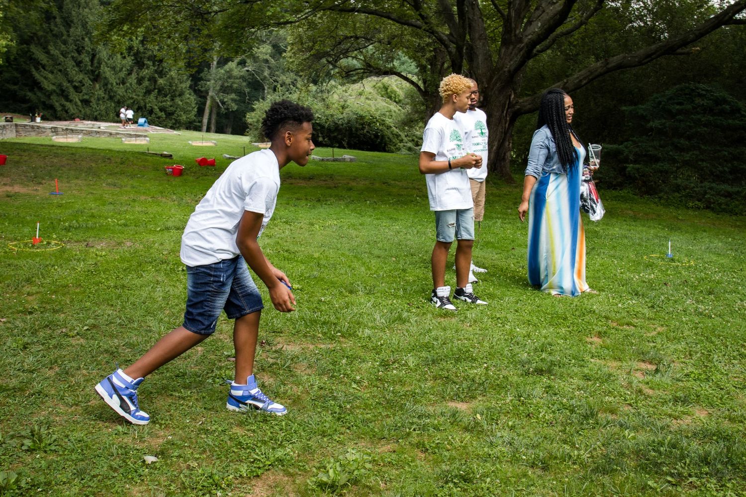 Three young people enjoy outdoor activities on a green lawn at a family reunion gathering.