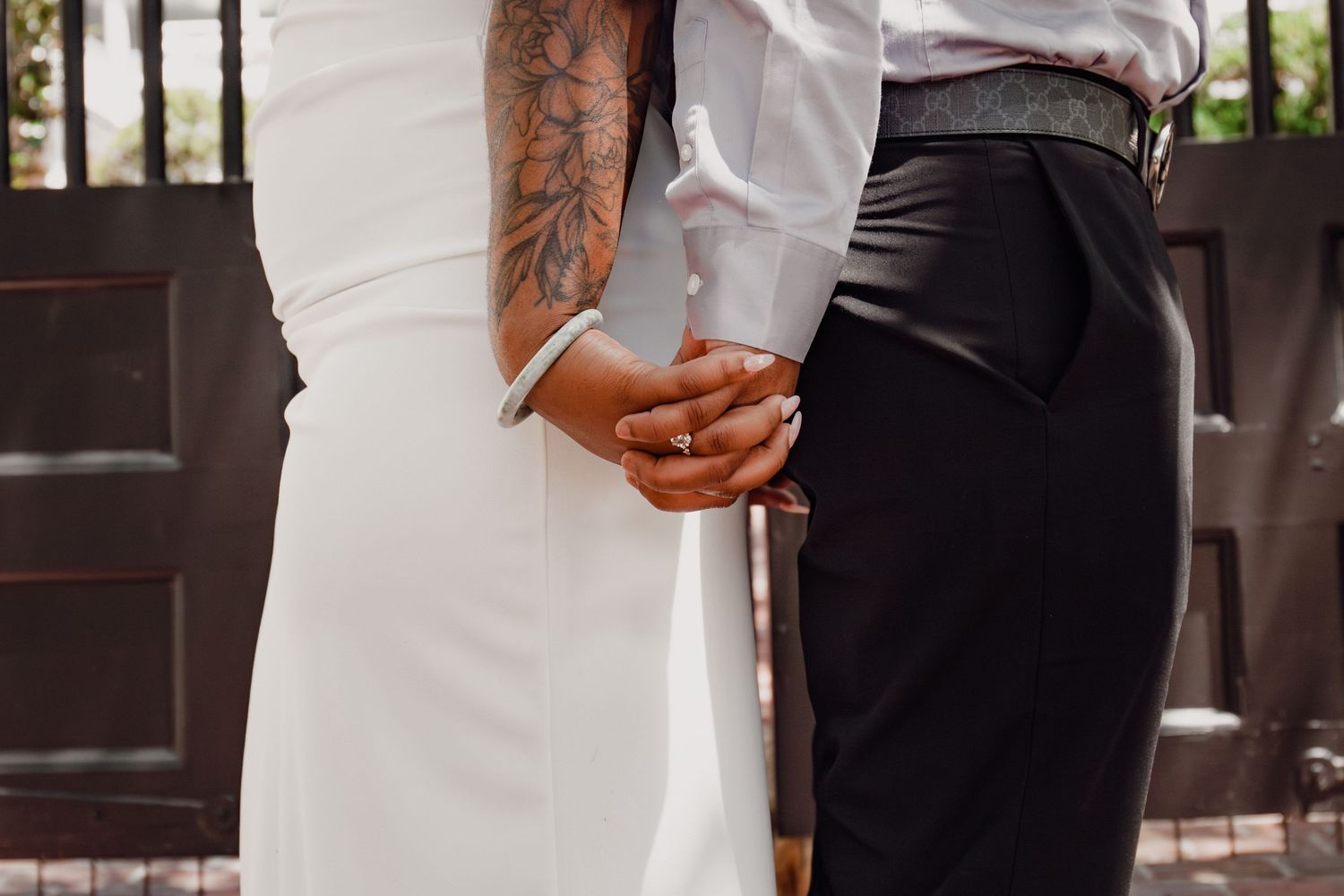 Bride in white gown and tattooed groom in black pants holding hands at outdoor wedding ceremony.