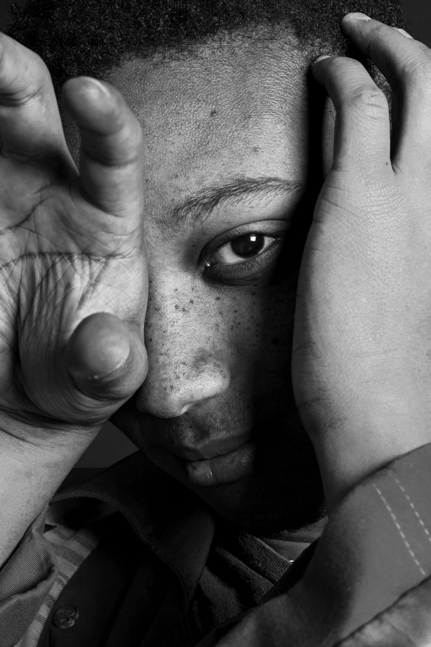 Black and white portrait of a young Black man with freckles holding hand up to his face.