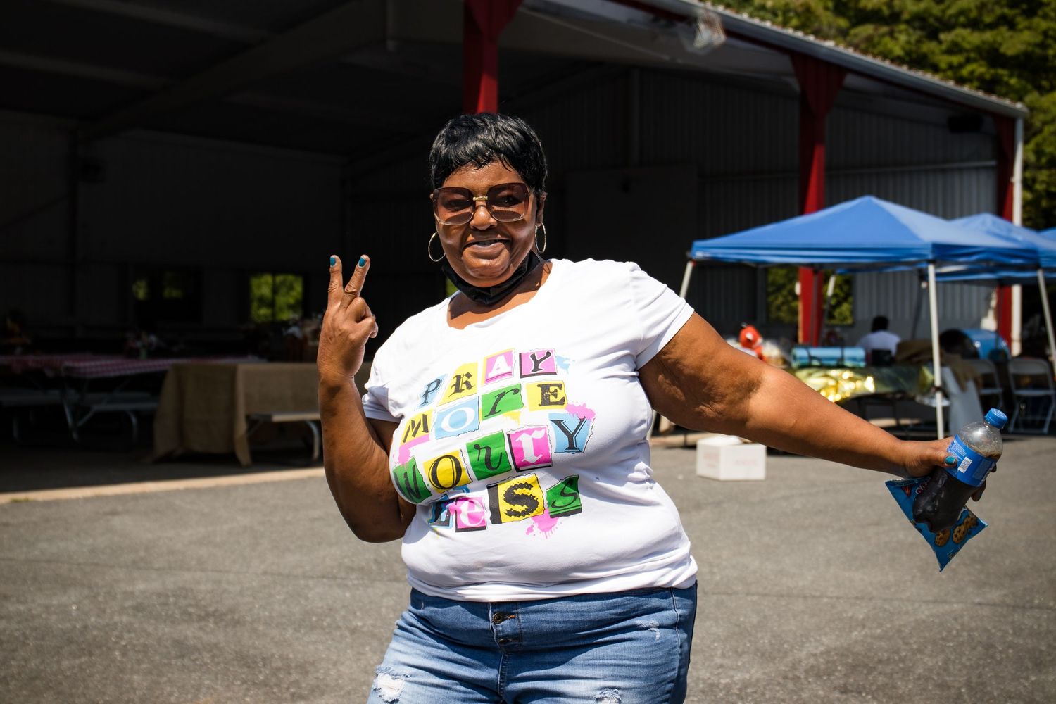 A woman in a colorful t-shirt makes a peace sign while smiling outdoors at an event.