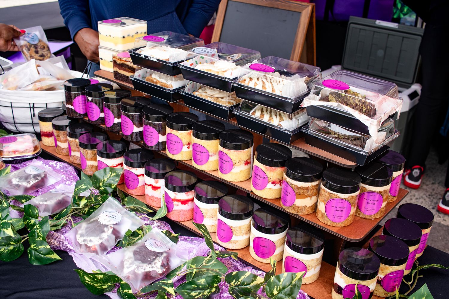Display of purple-labeled jars and packaged baked goods arranged on tiered wooden shelves.