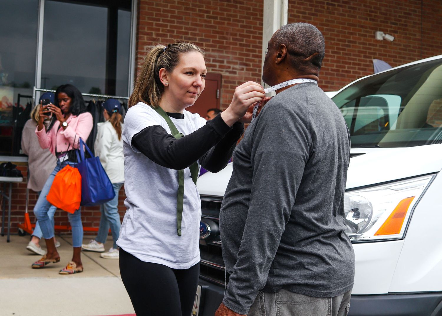 A woman in a white shirt pins a badge onto a man outside a community center building.