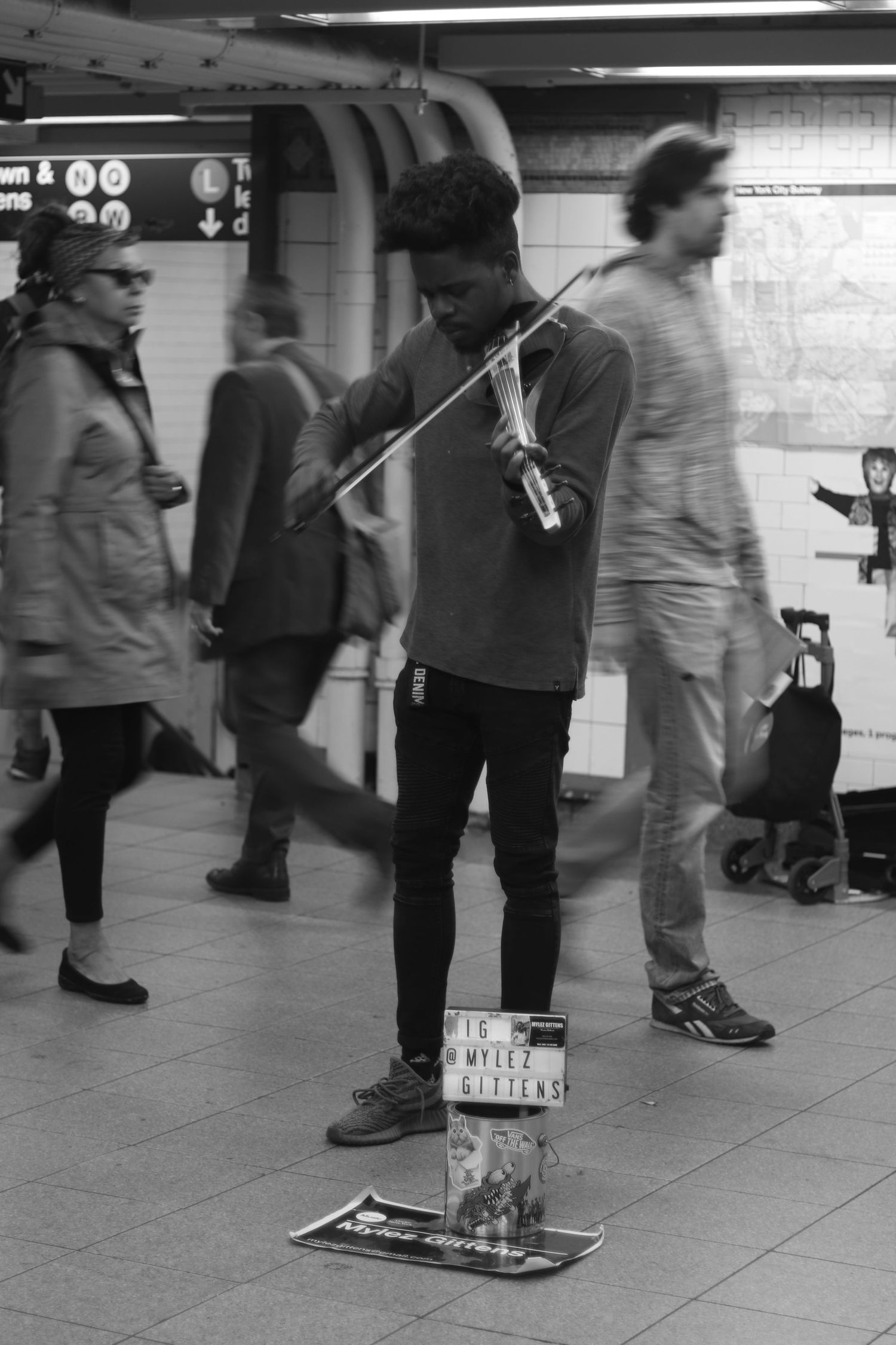 Black and white photo of a street musician playing violin in a busy New York City subway station.