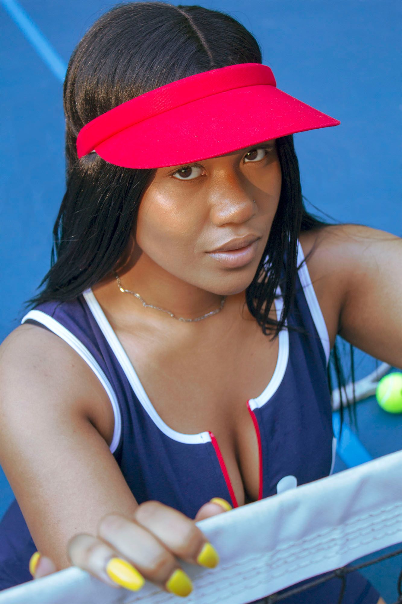 A Black woman in a navy tennis outfit and red visor holds a racket on a blue tennis court.