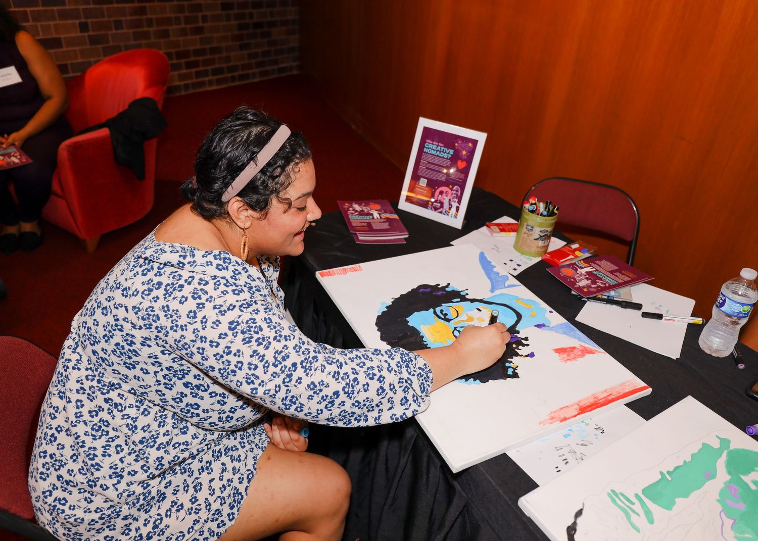 Artist painting a colorful portrait at a creative event with art supplies on table.