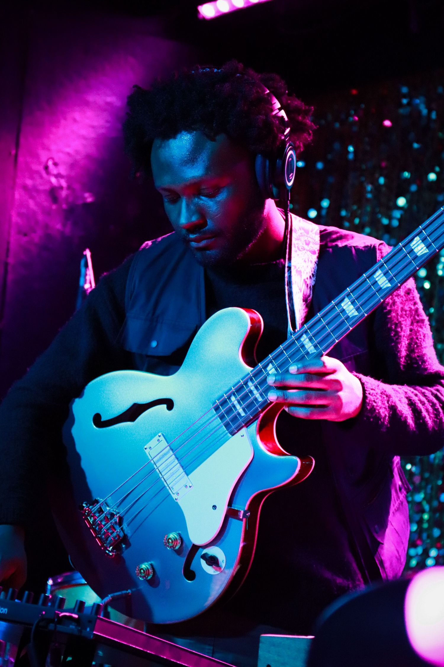 Male guitarist playing white semi-hollow electric guitar under purple and blue stage lighting.