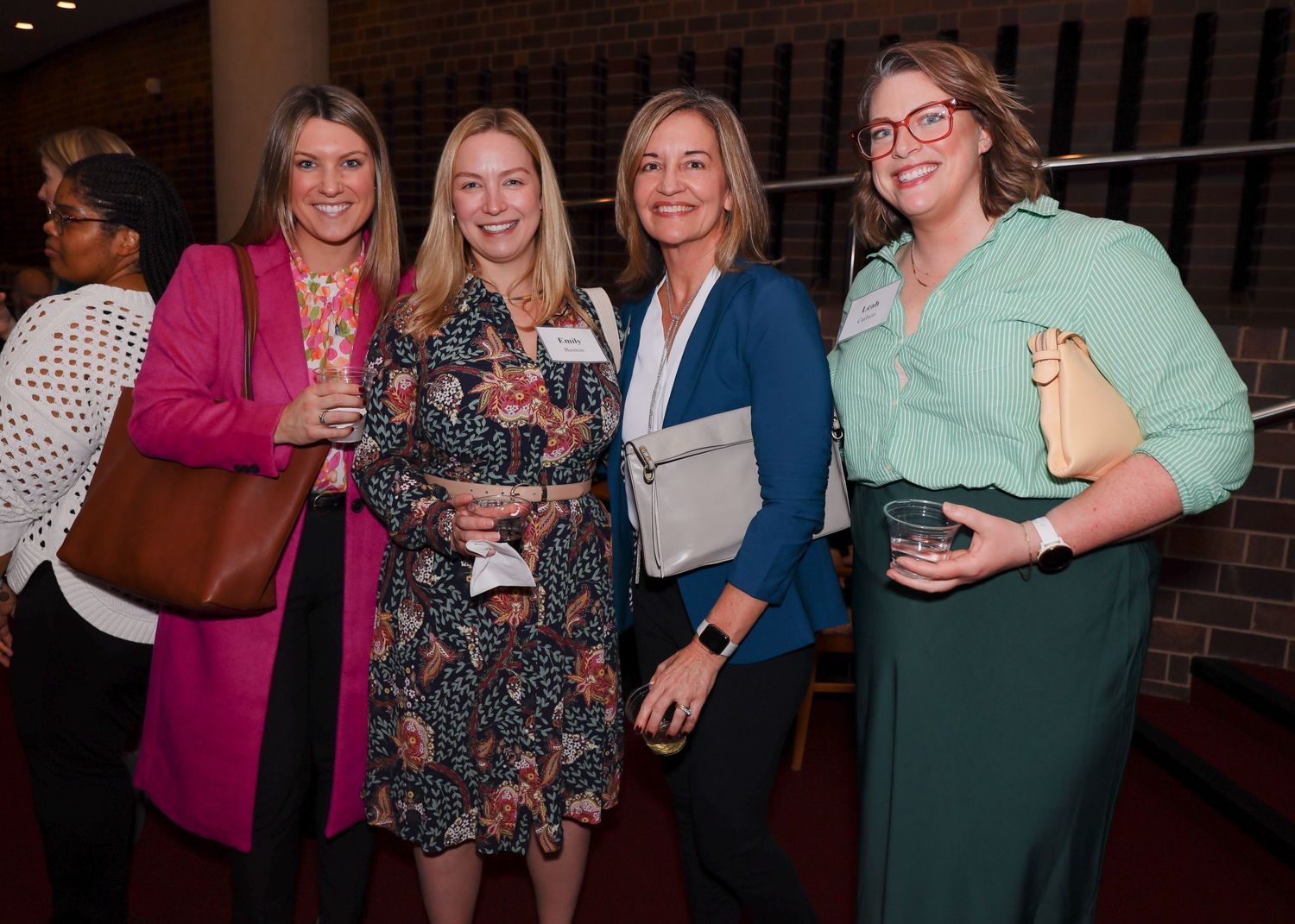 Four smiling women posing together at an indoor awards or networking event.
