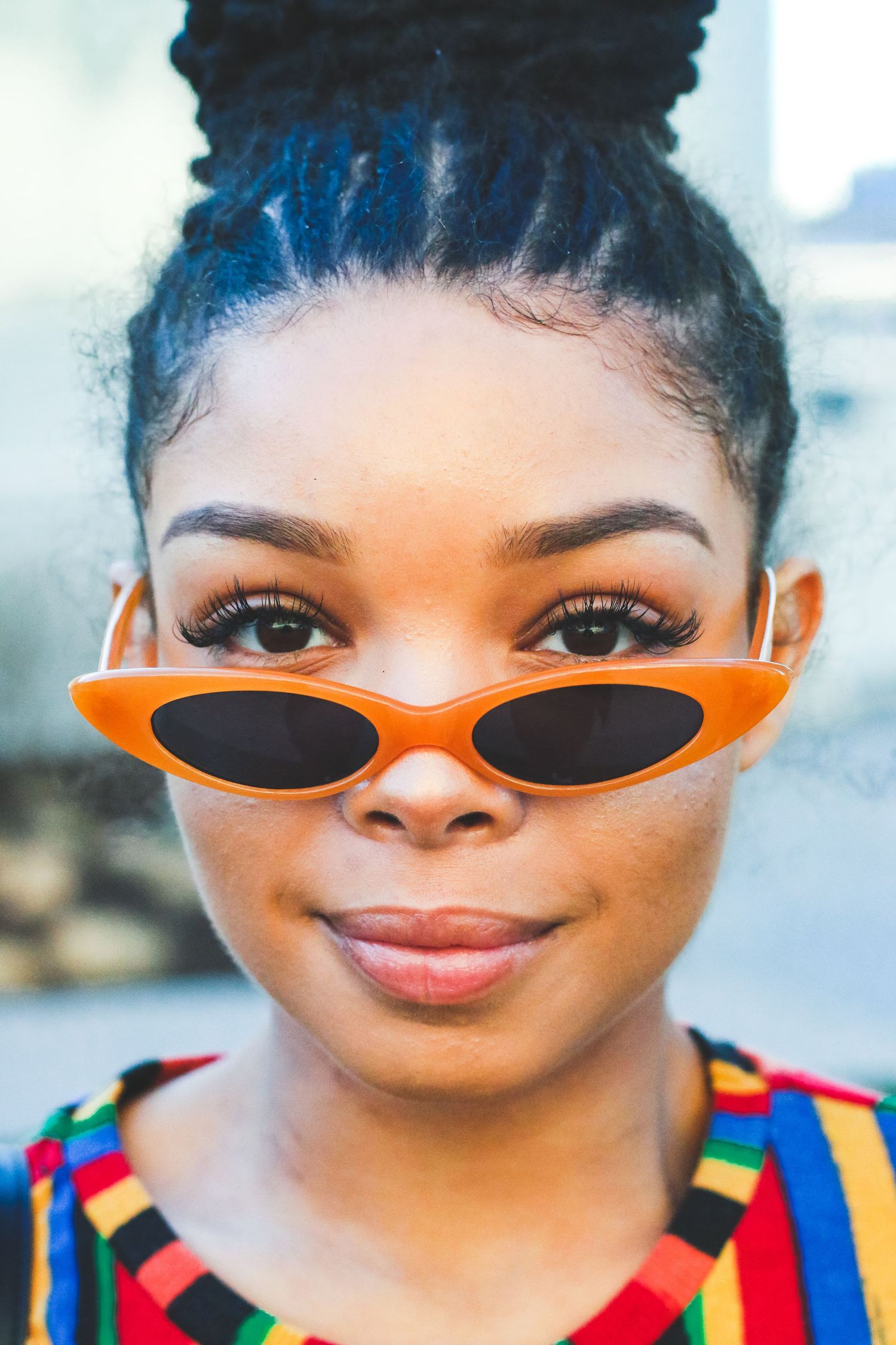 Young Black woman wearing orange cat-eye sunglasses and colorful striped top.