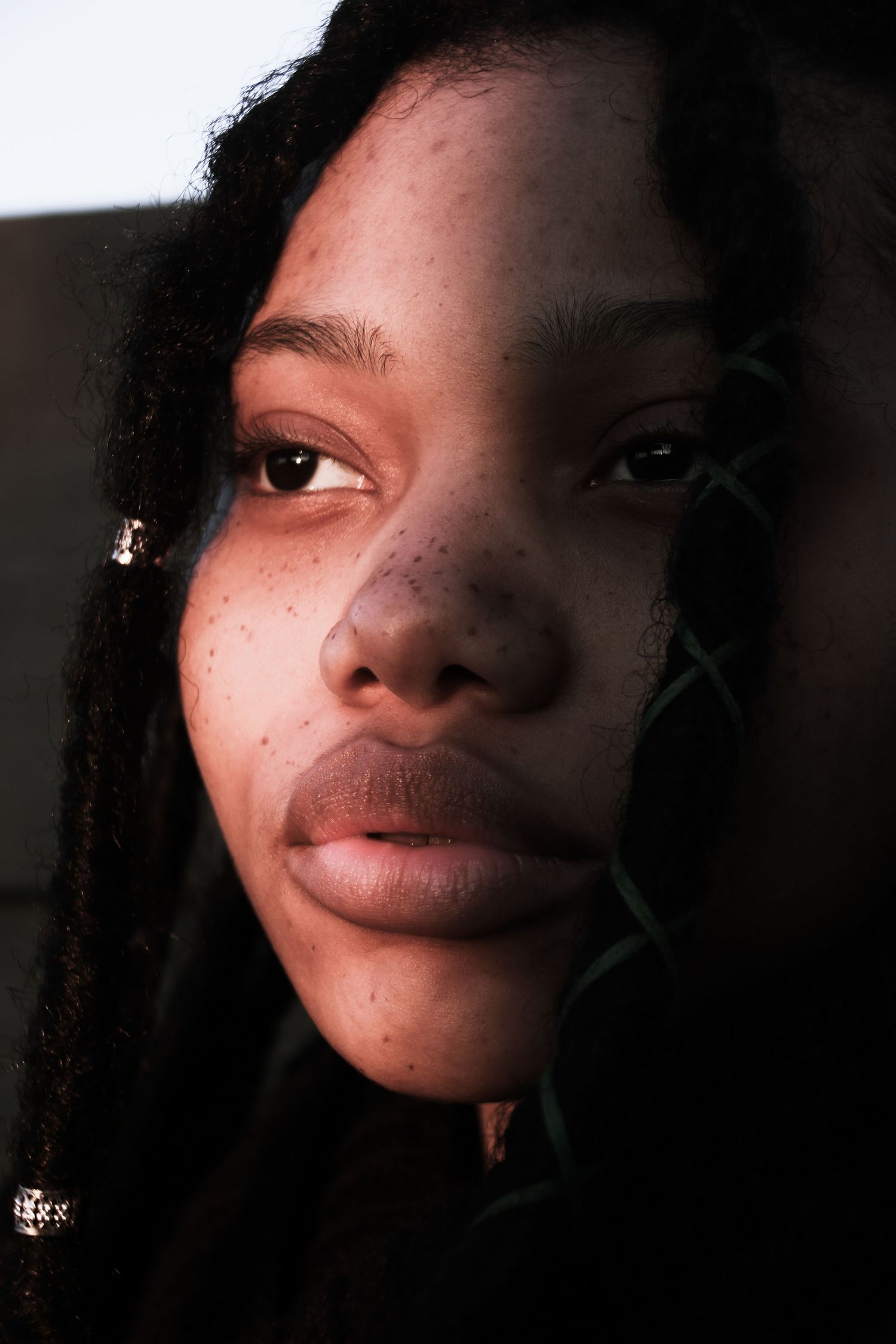 Close-up portrait of young woman with freckles and locs in dramatic shadow lighting.