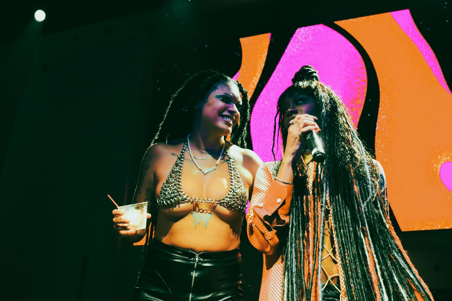 Two female artists sharing a moment on stage together during a colorful live music performance.