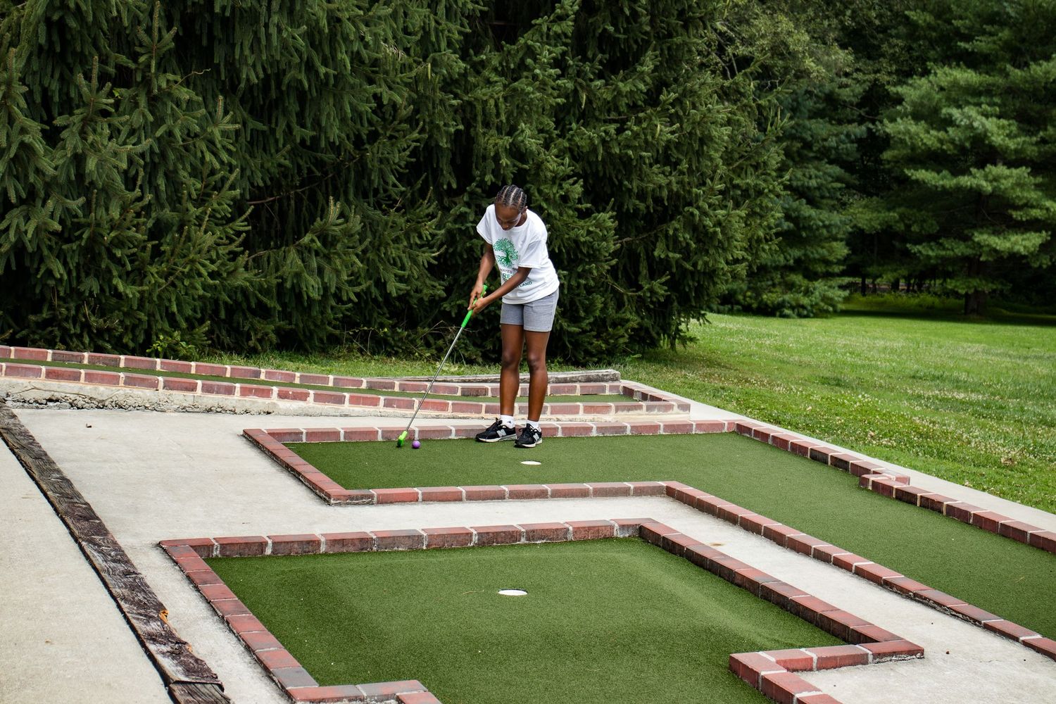 A young woman concentrates while playing miniature golf on a well-maintained outdoor course.
