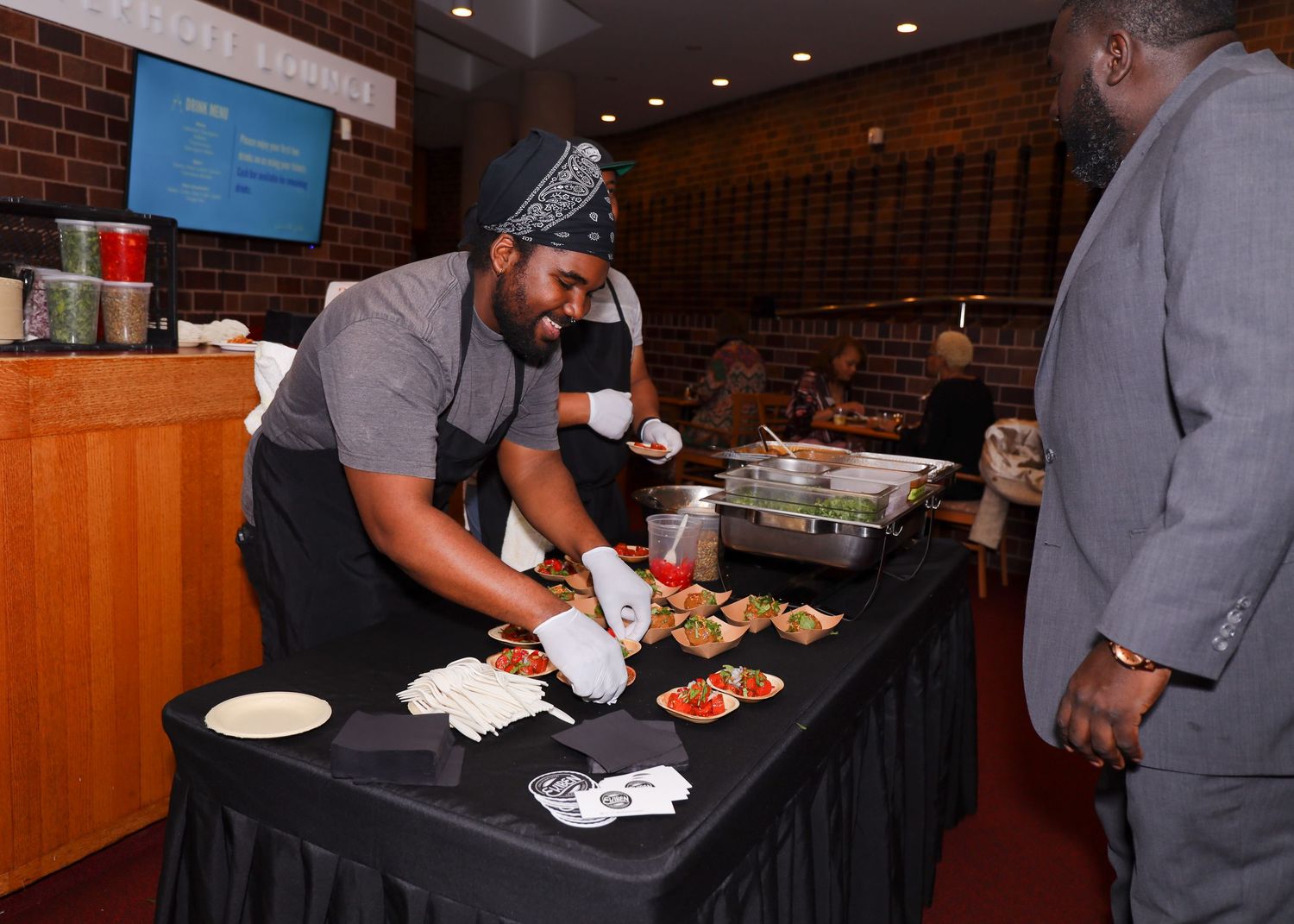 Chef in gray uniform serving food at a catered event buffet table.