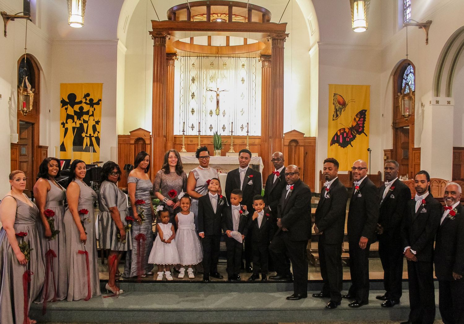 Wedding party posing inside a church with bridesmaids in silver dresses and groomsmen in black suits.