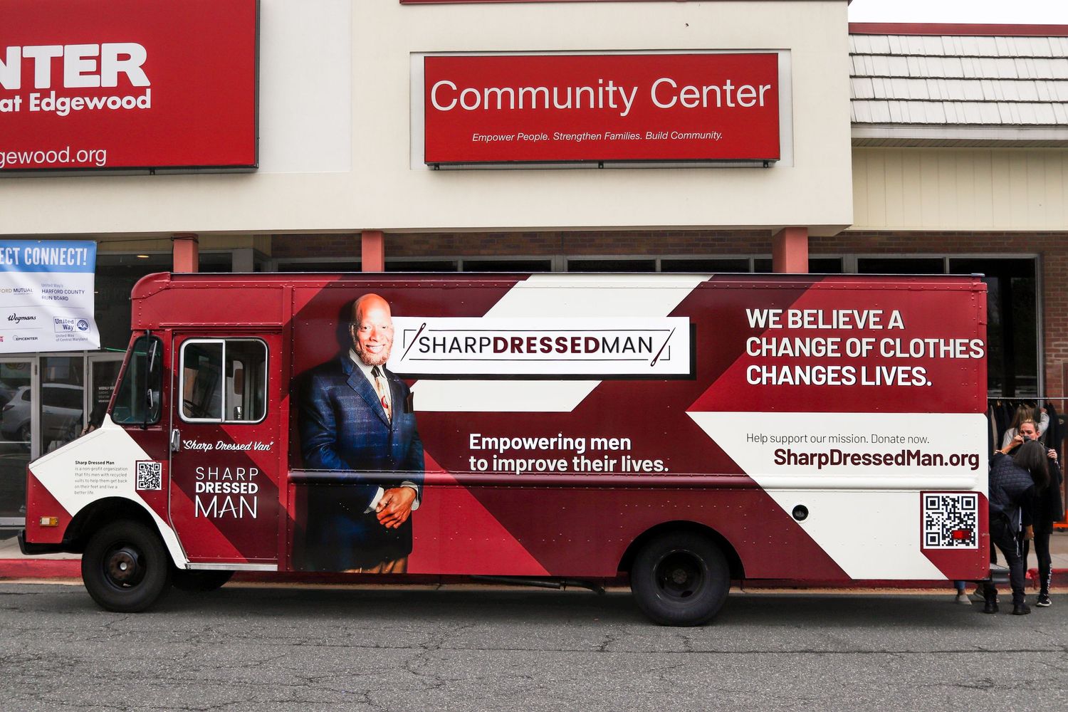 A Sharp Dressed Man charity truck parked outside a community center empowering men with clothing.