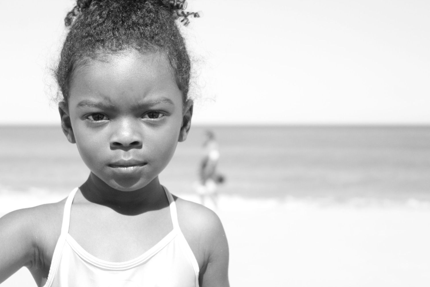 Black and white portrait of young Black girl with serious expression at sunny beach.