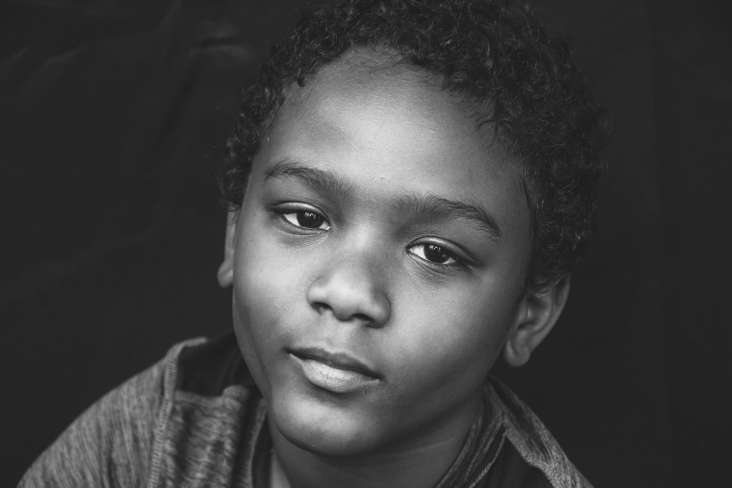 Black and white portrait of a young Black boy with short hair looking pensively at the camera.