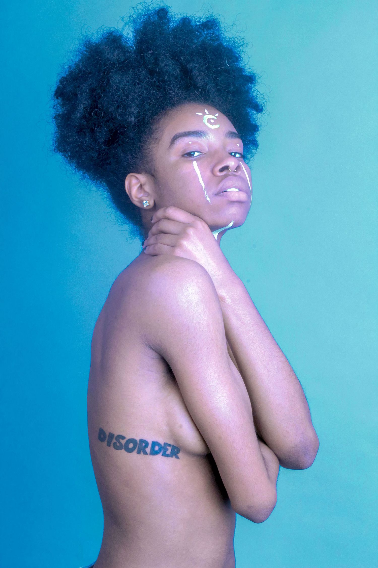 Black woman with afro hair and DISORDER arm tattoo posing against blue background.