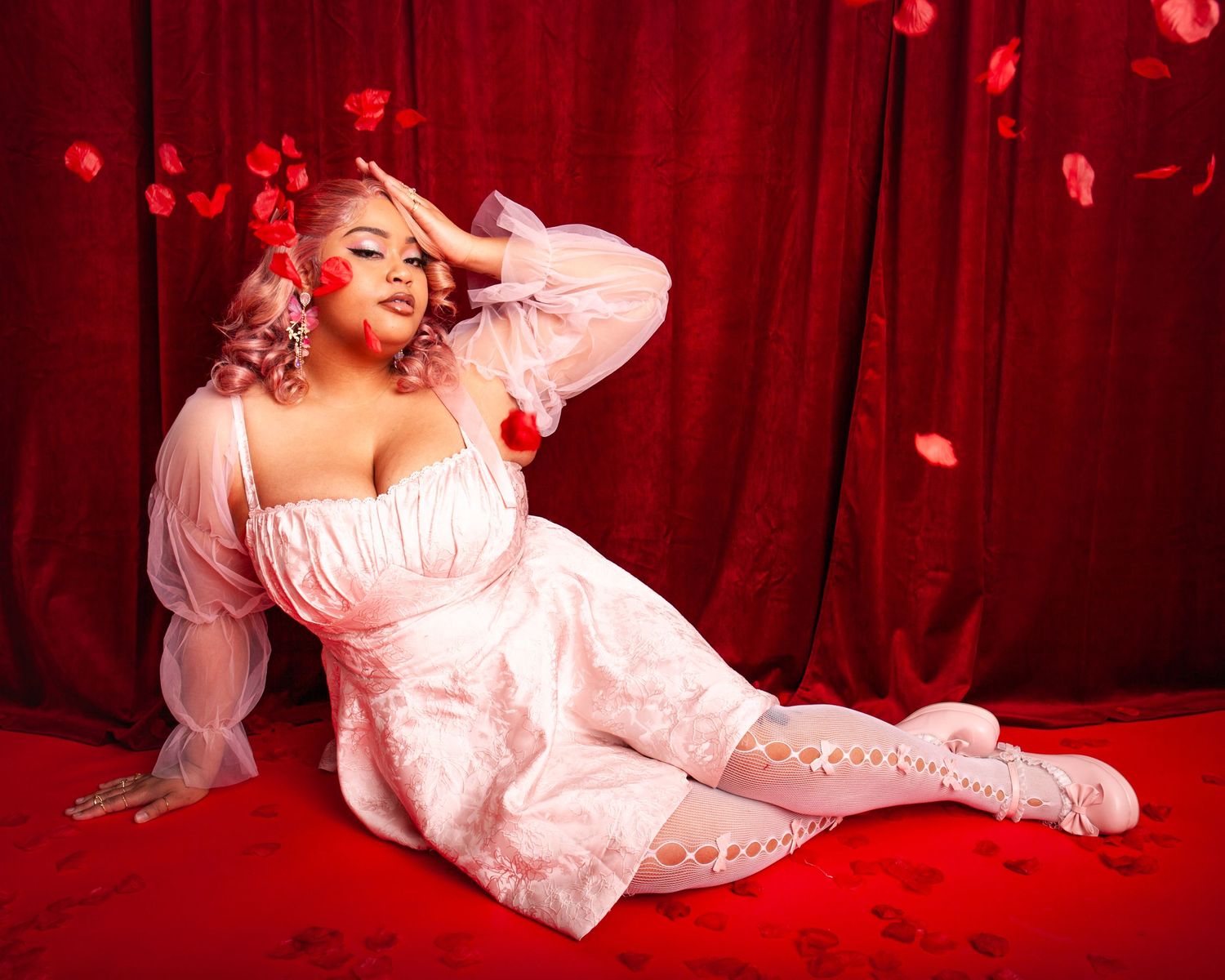 woman in white corset gown poses on red floor with falling rose petals background.