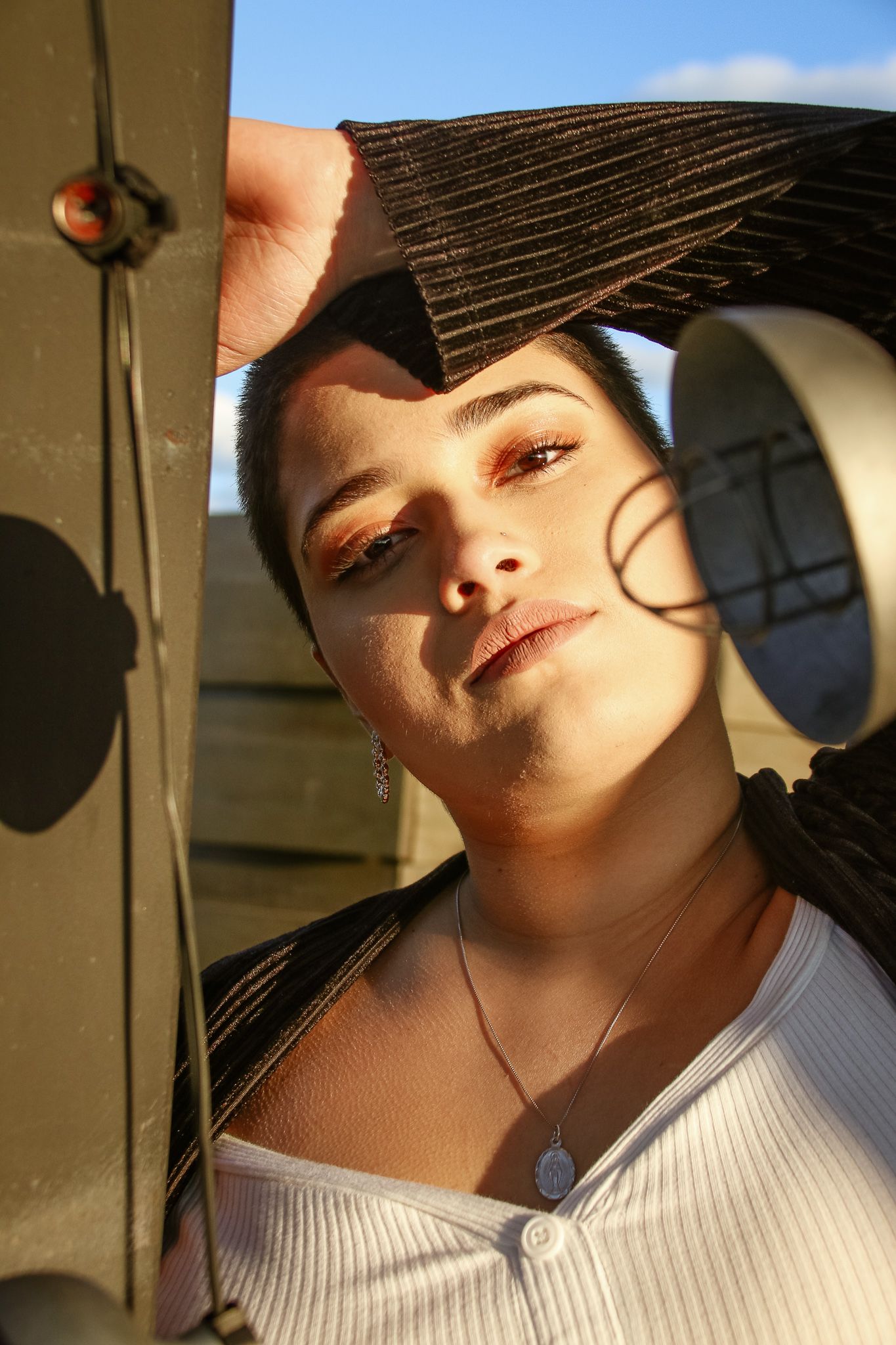 Young woman posing outdoors in golden hour light with dramatic eye makeup.