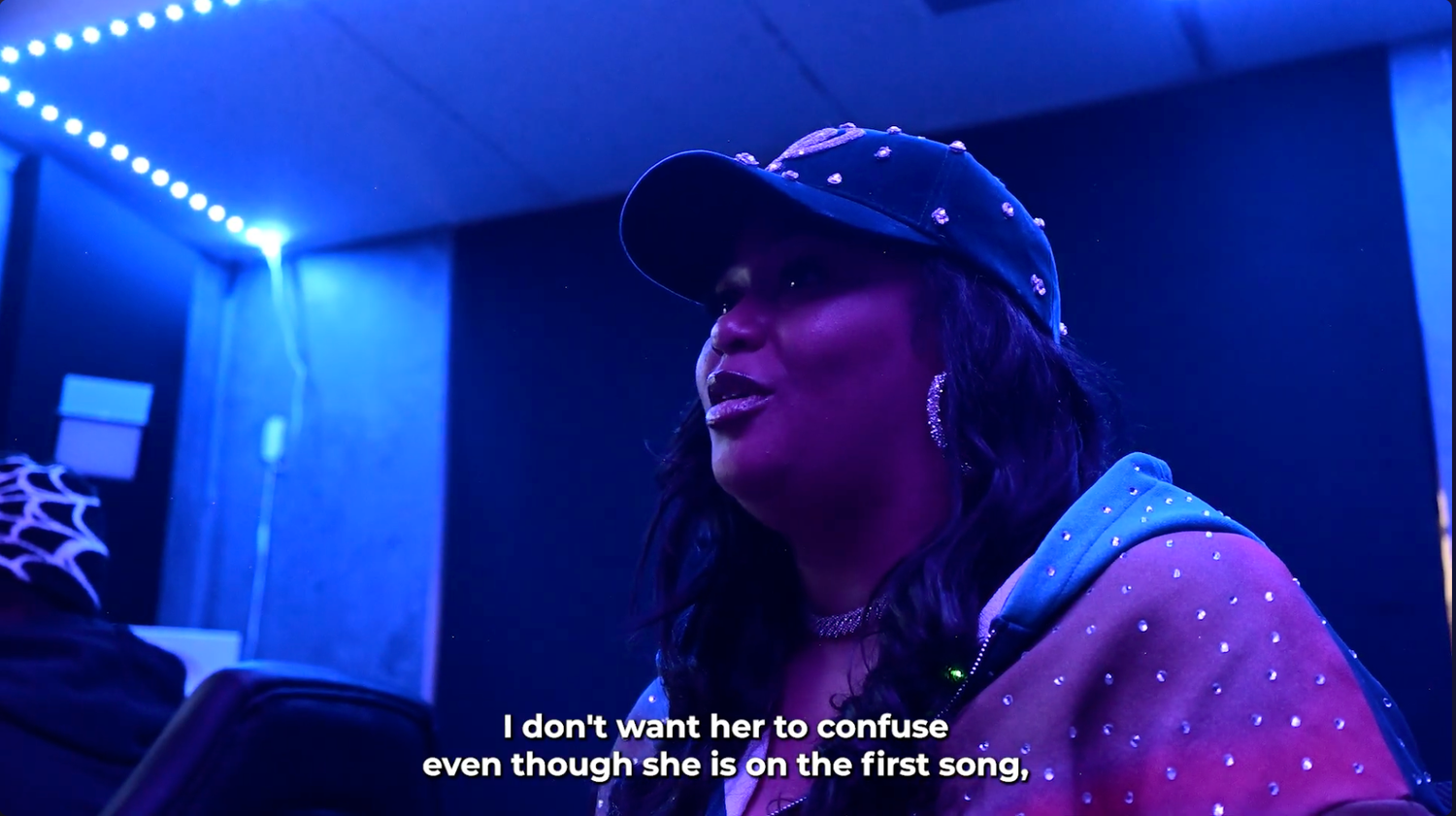 Woman in baseball cap speaks in neon-lit studio with subtitle about not wanting to confuse someone on the first song.