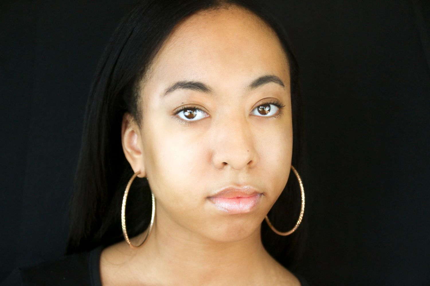 Close-up portrait of a young woman with hoop earrings against a dark background.
