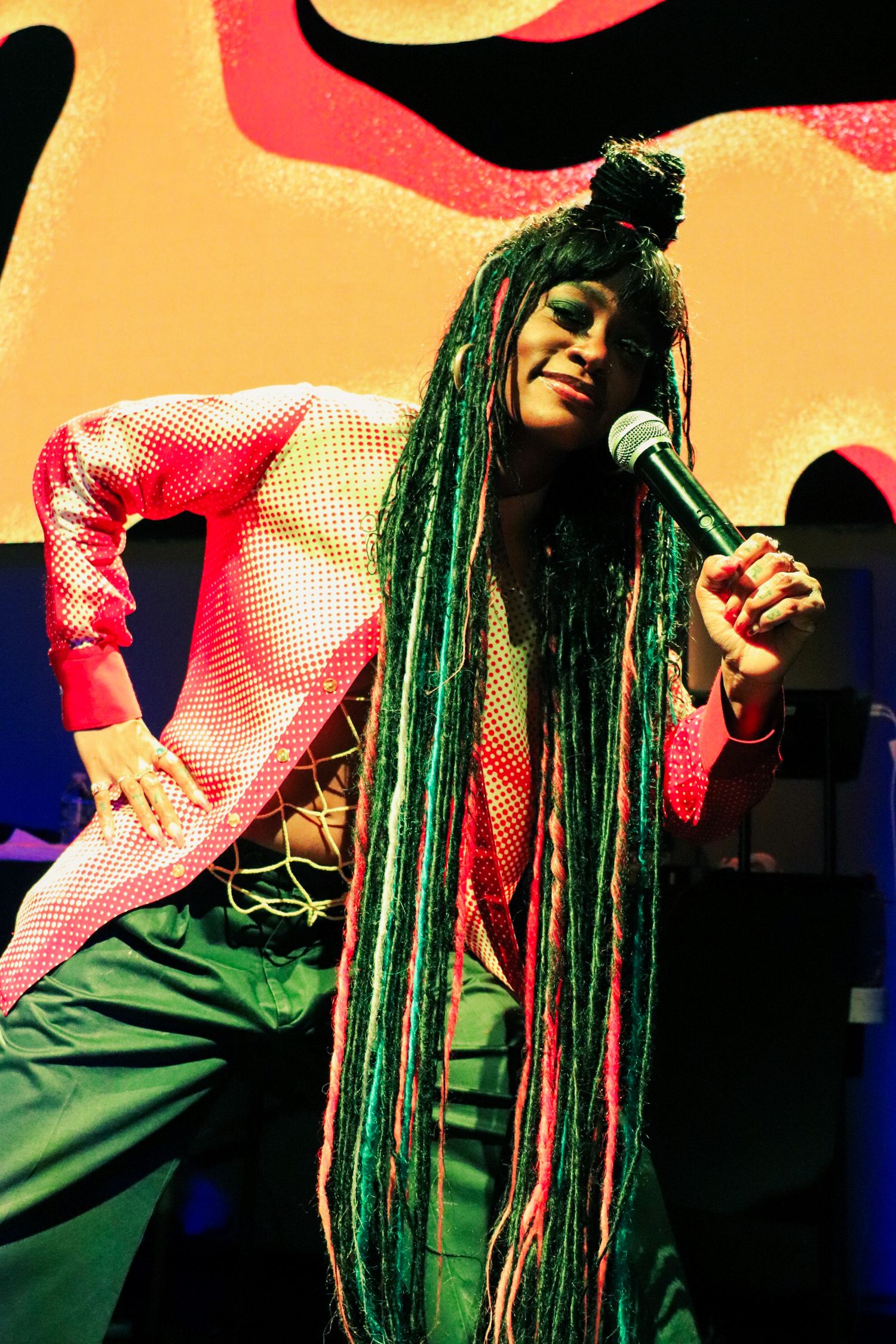 Colorful performer singing into microphone on stage.