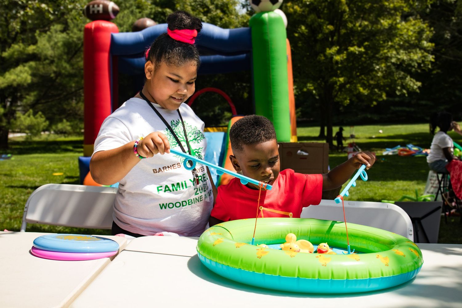 Two children play a duck fishing game at an outdoor family fun day community event.